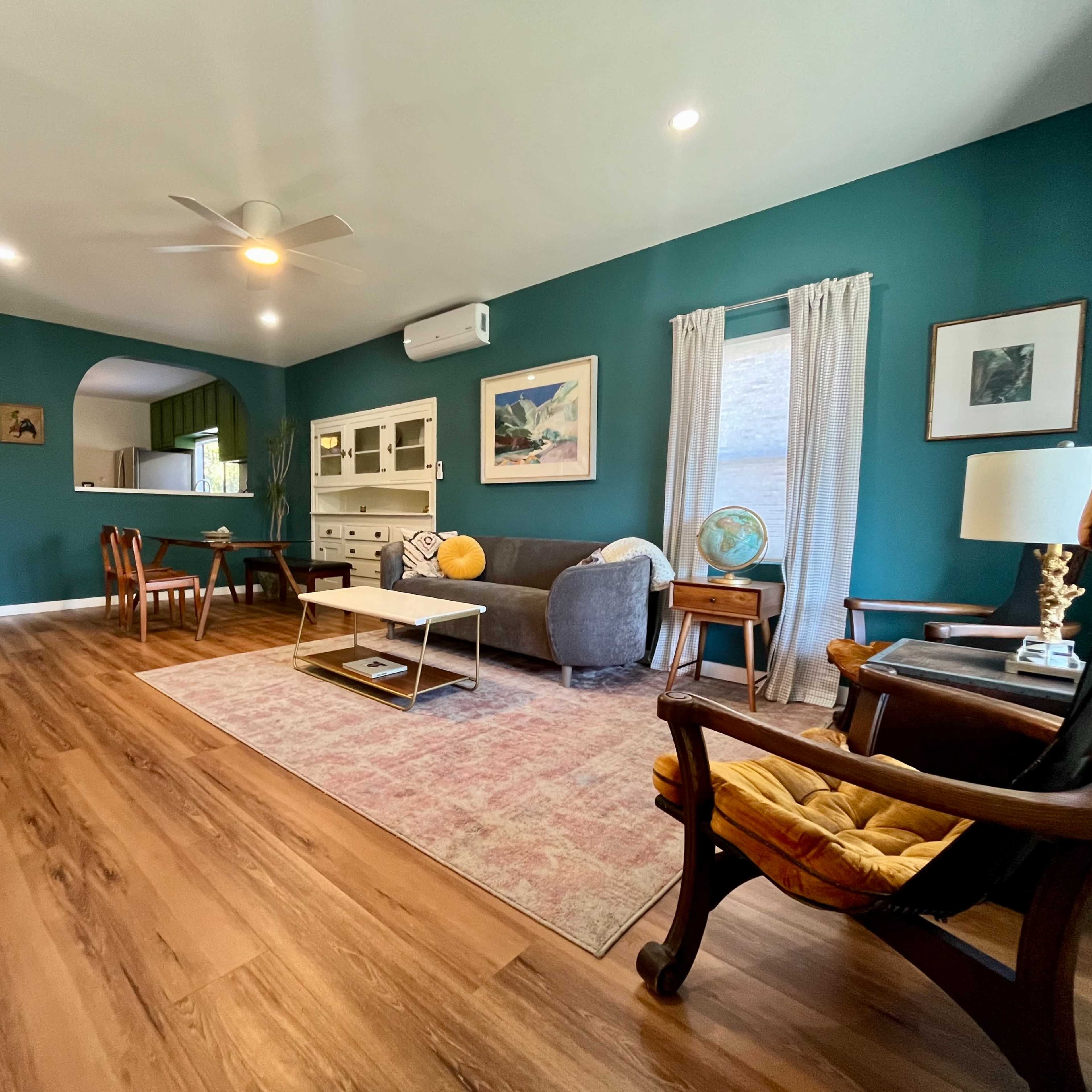 A living room features a combination of modern and vintage furnishings, with green walls, a large area rug, and a mix of seating options.