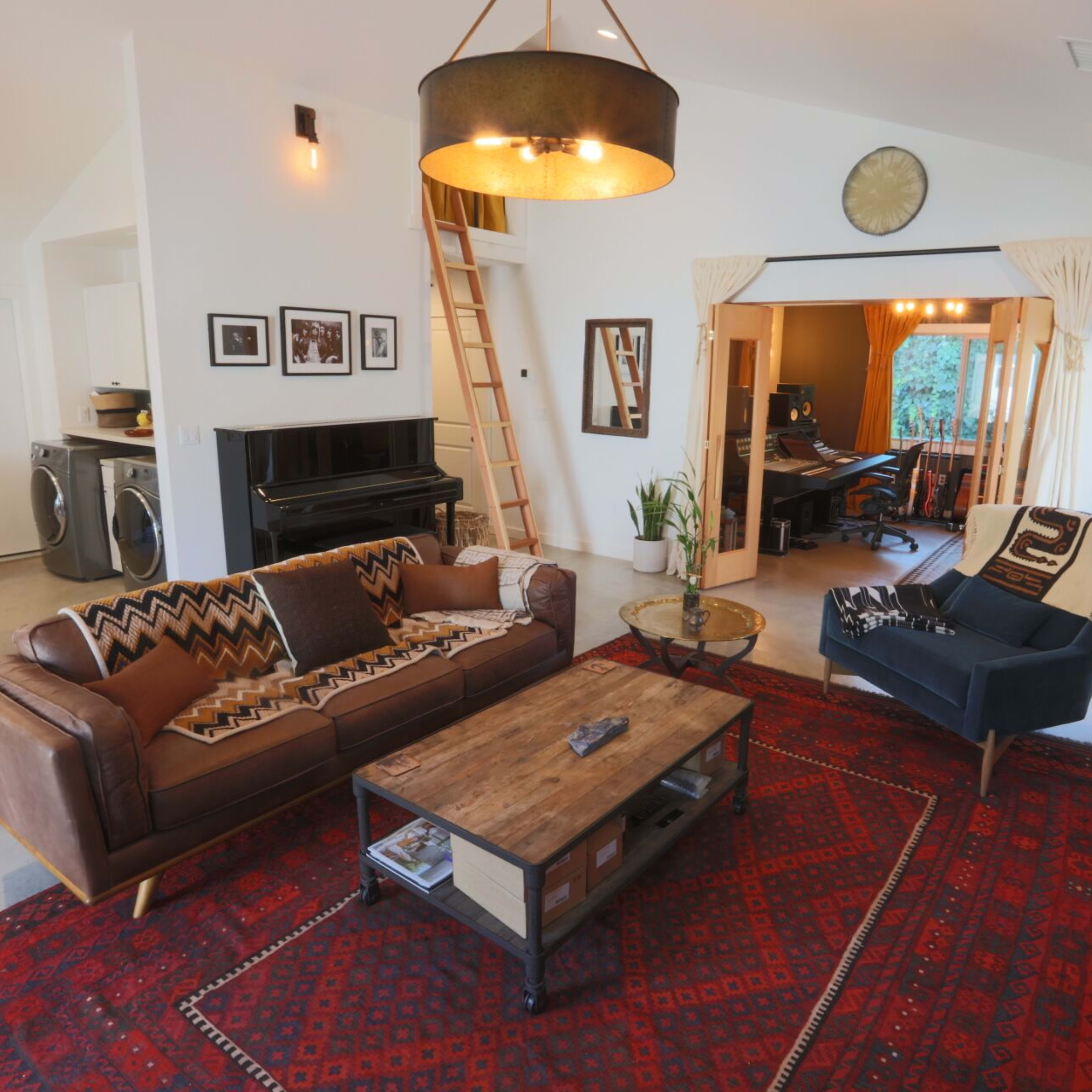A cozy living room features a brown leather sofa, a wooden coffee table, and a patterned rug, with a piano and open doorway leading to a music area.