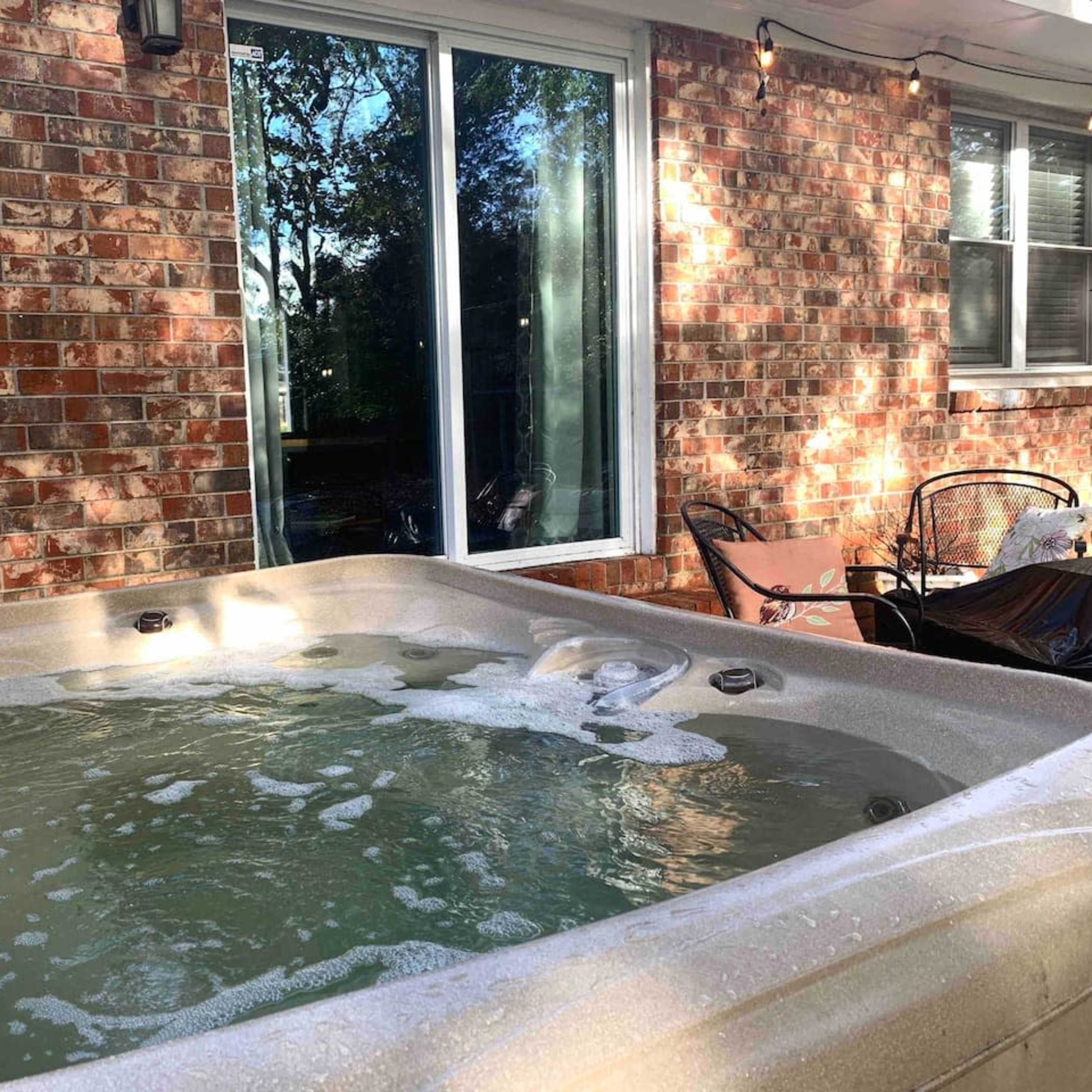 A hot tub with bubbles is positioned next to a brick wall and a large glass sliding door.