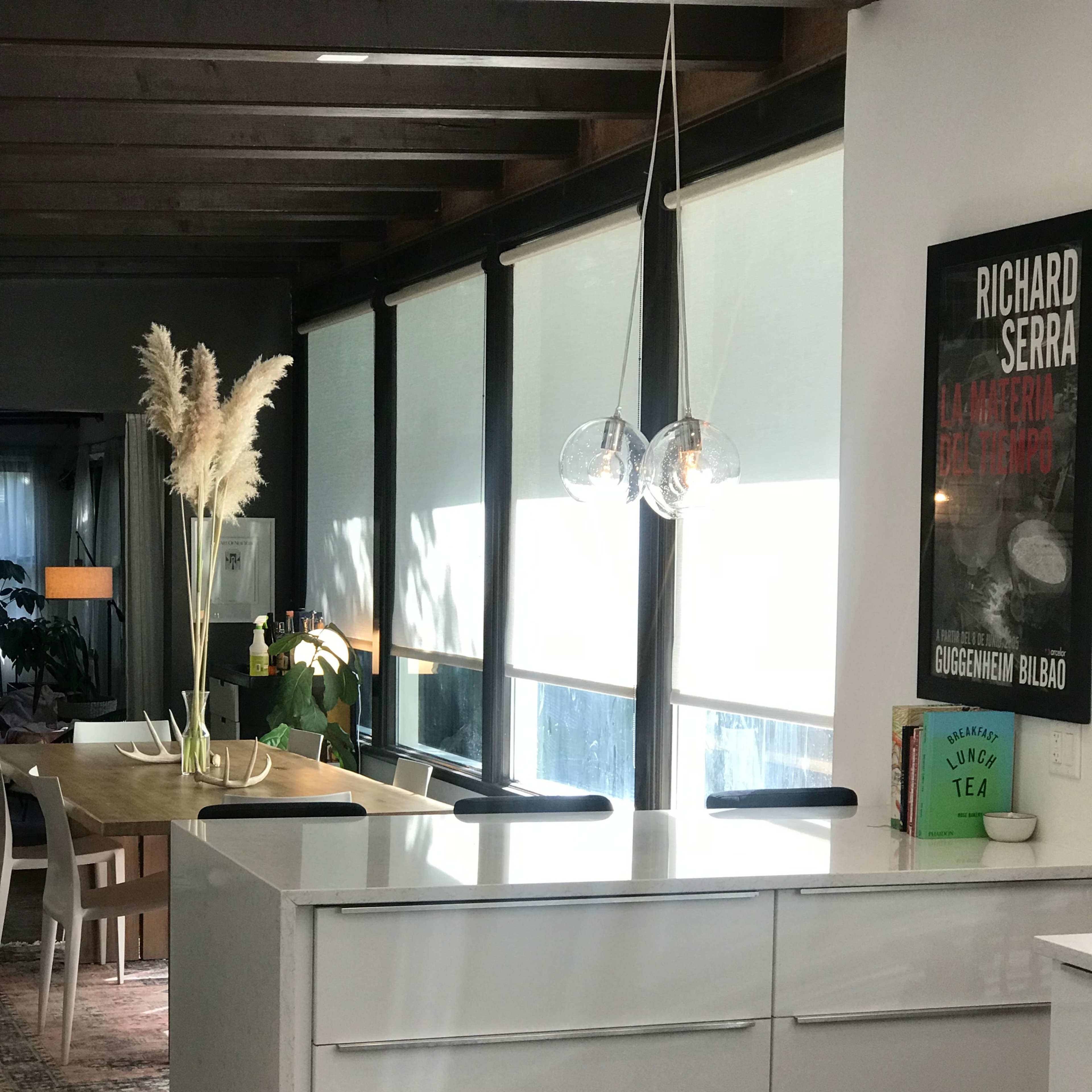 A modern kitchen with a white island and drawers, large windows allowing natural light, and a dining area in the background.