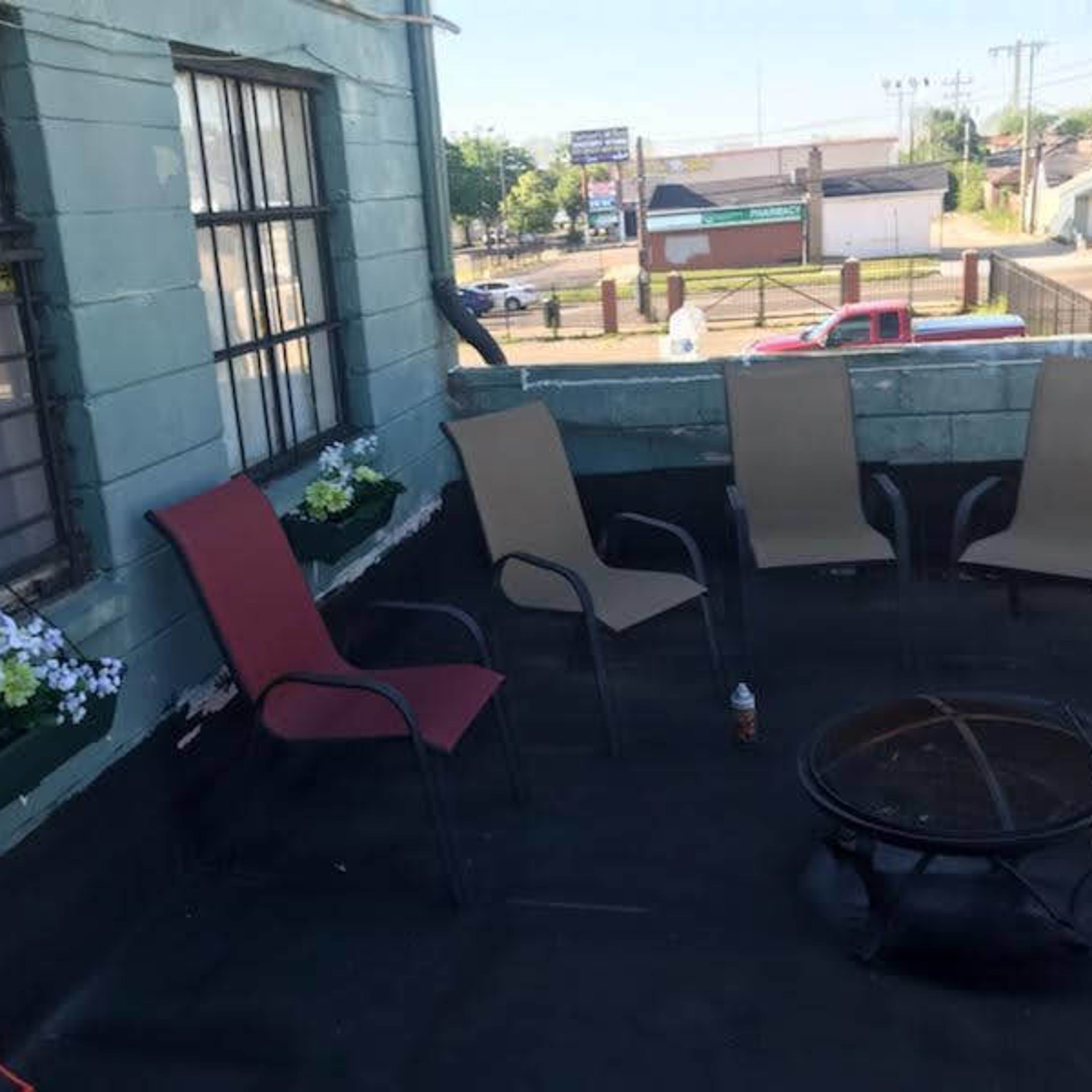A rooftop space with several chairs arranged around a fire pit and potted flowers near the windows.