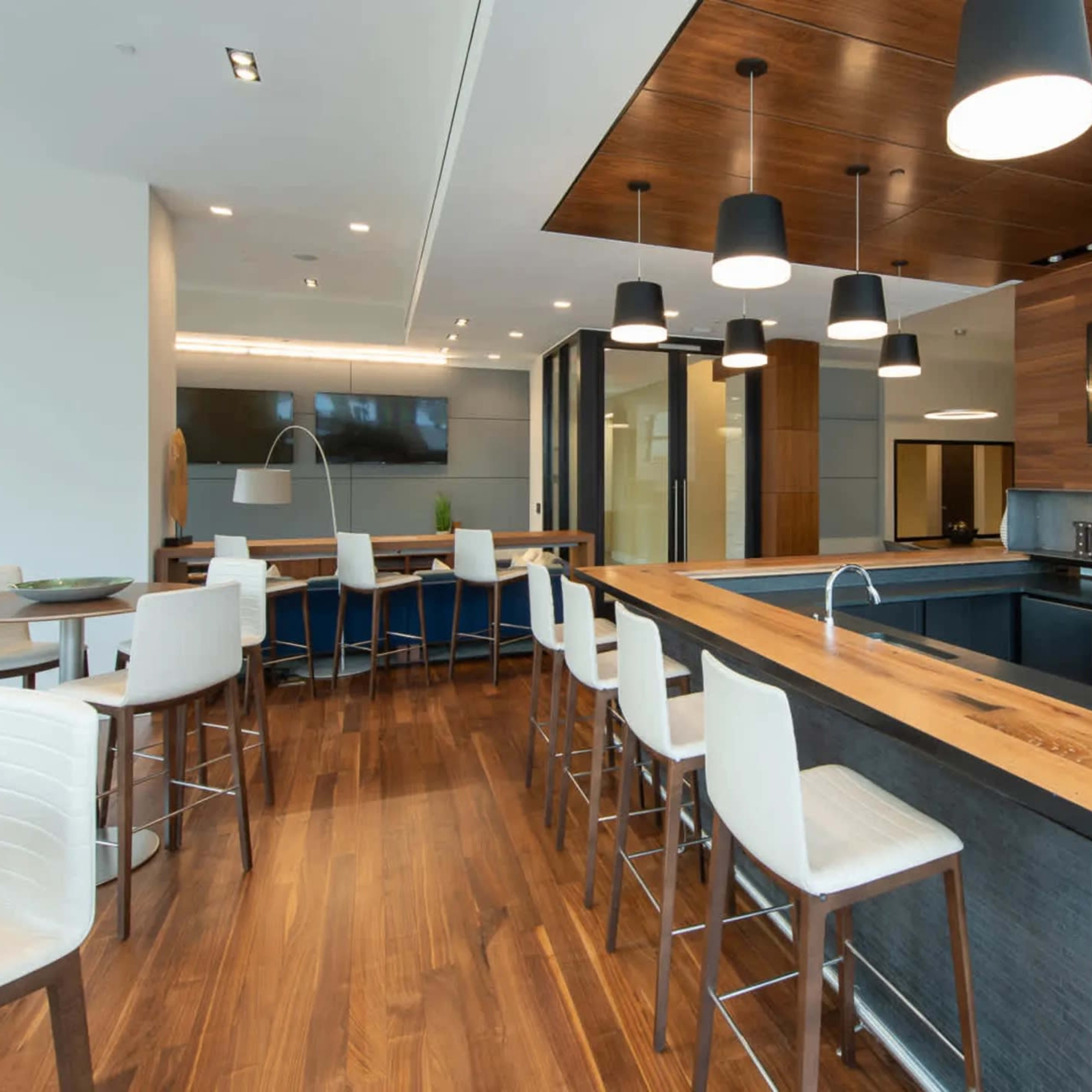 A modern kitchen with a wooden central island, white bar stools, pendant lighting, and dark cabinetry.