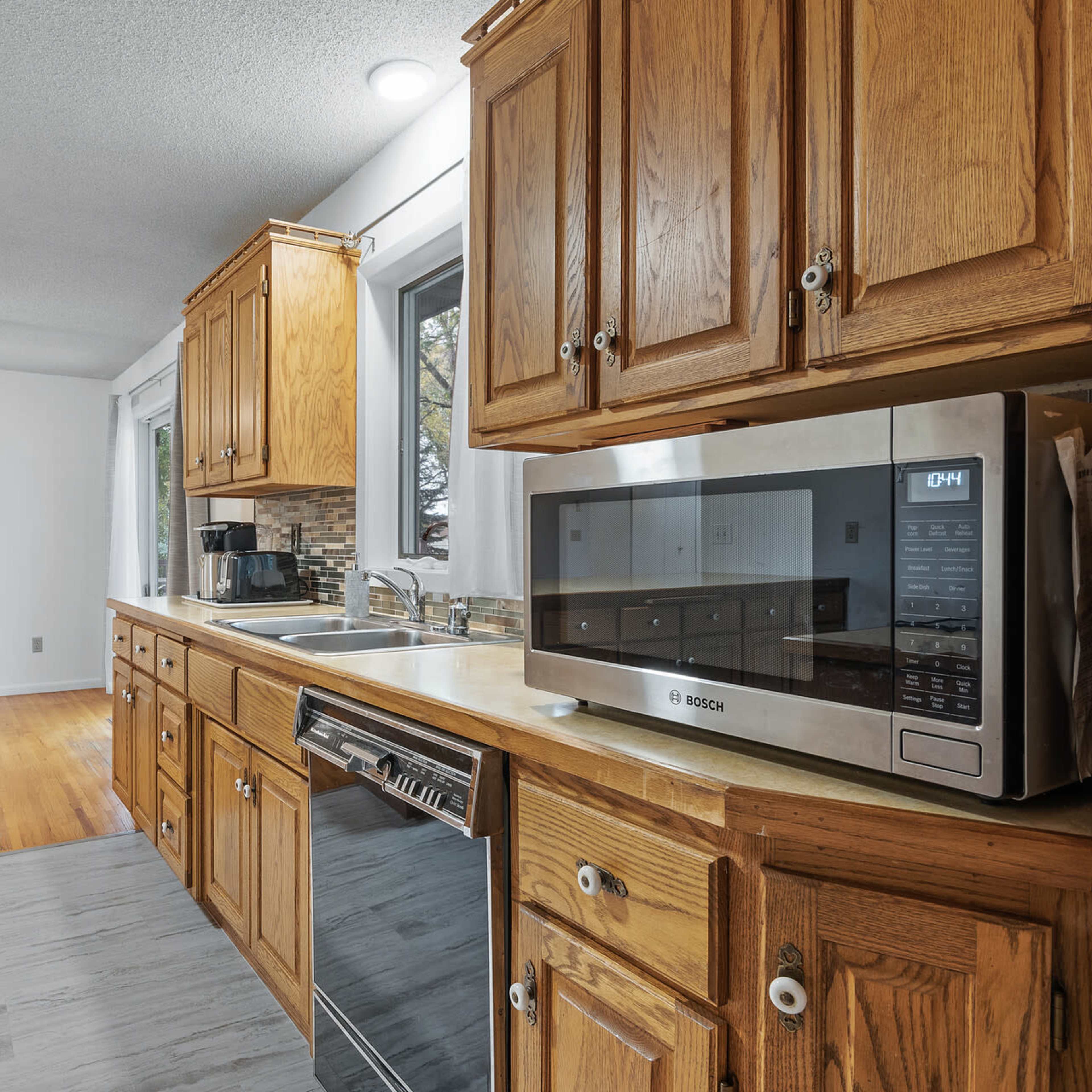 A modern kitchen with wooden cabinets, stainless steel appliances, and a dining area visible in the background.