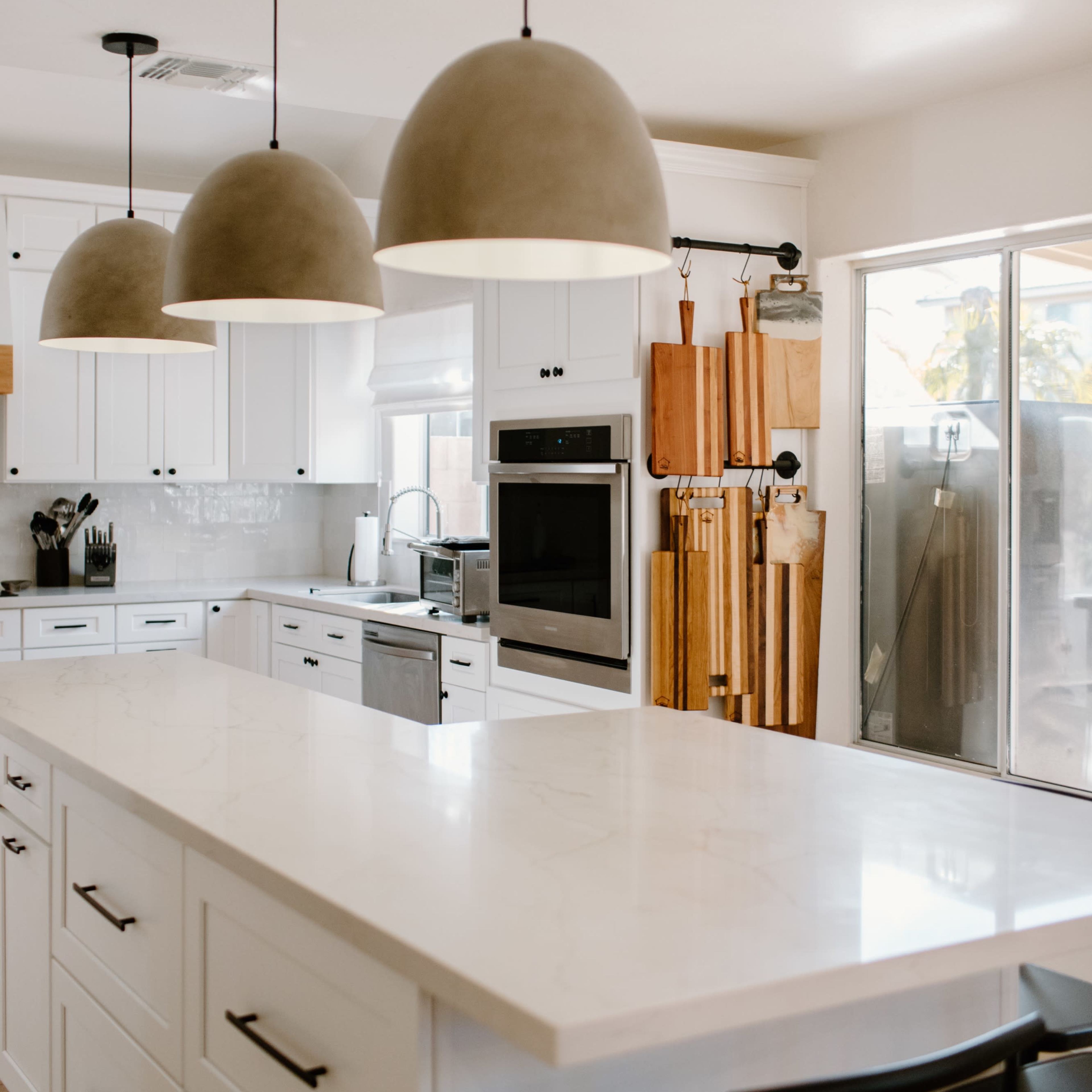 A modern kitchen features white cabinetry, a large island with a marble countertop, and three pendant lights hanging above.