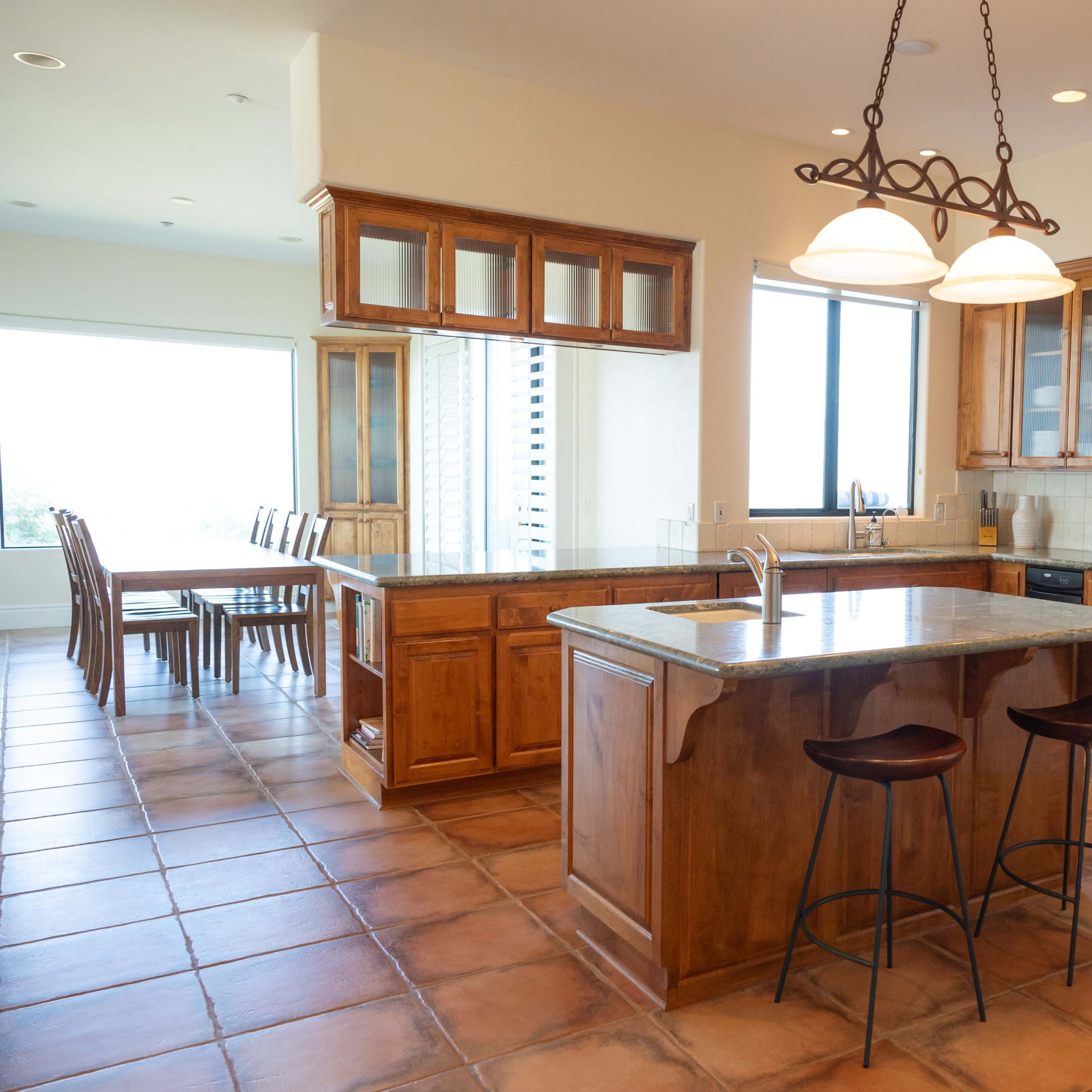 A spacious kitchen with wooden cabinetry, a large island with two stools, and a window overlooking a dining area.