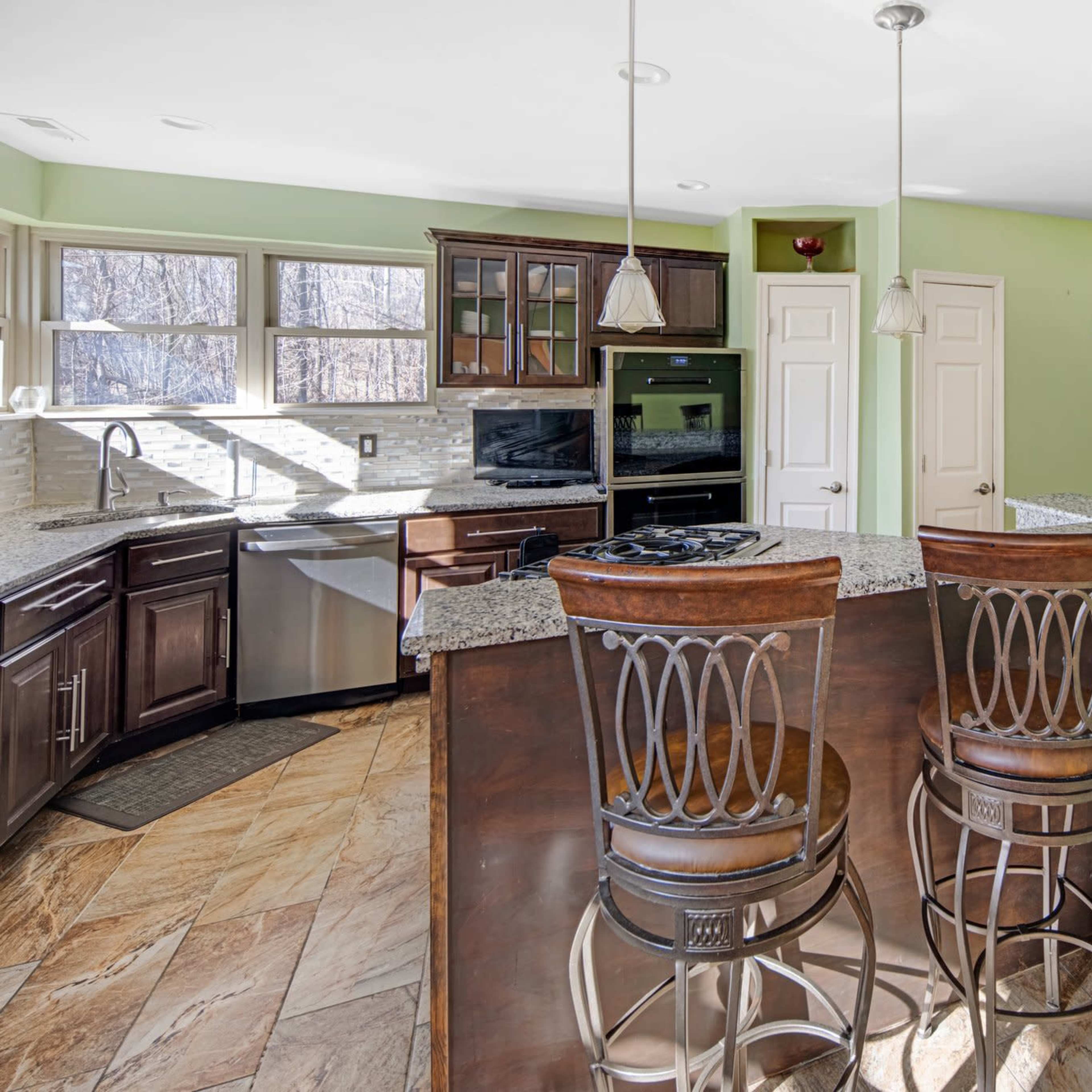 A modern kitchen with dark wooden cabinetry, granite countertops, and a breakfast bar with three high-backed stools.