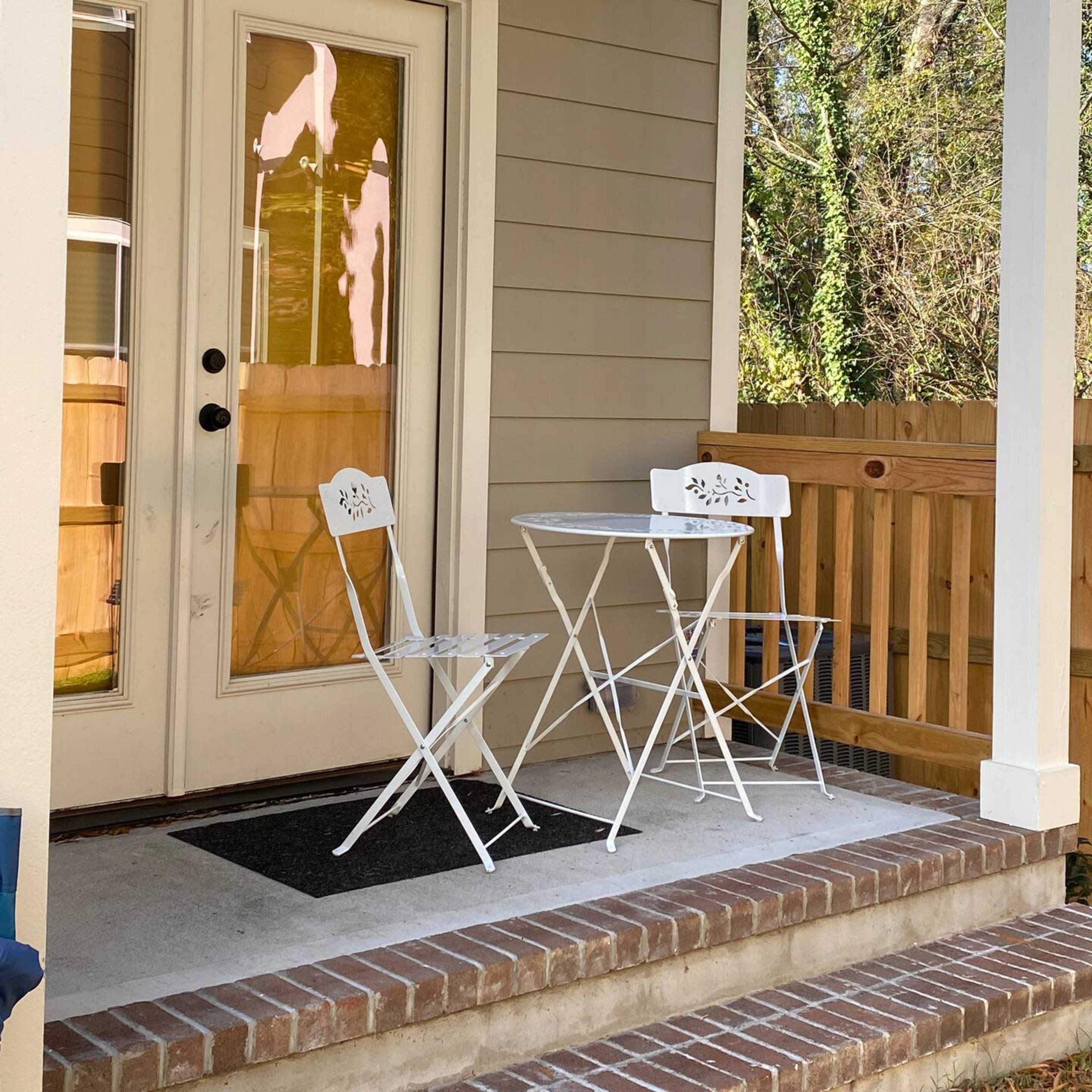 A small porch features a white bistro table and two chairs beside a set of glass doors leading inside.