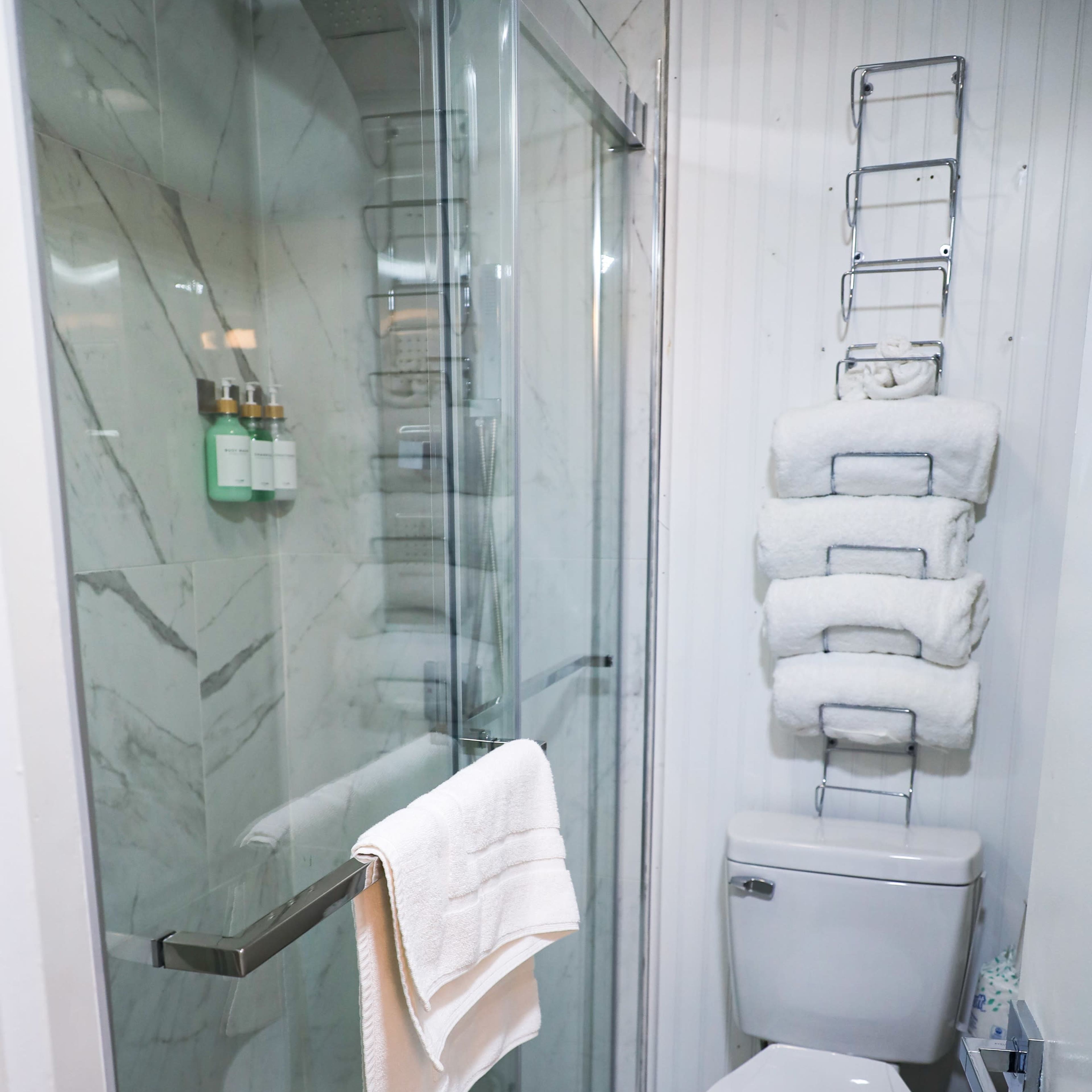 A bathroom featuring a glass shower stall, a toilet, and neatly stacked white towels on a towel rack.
