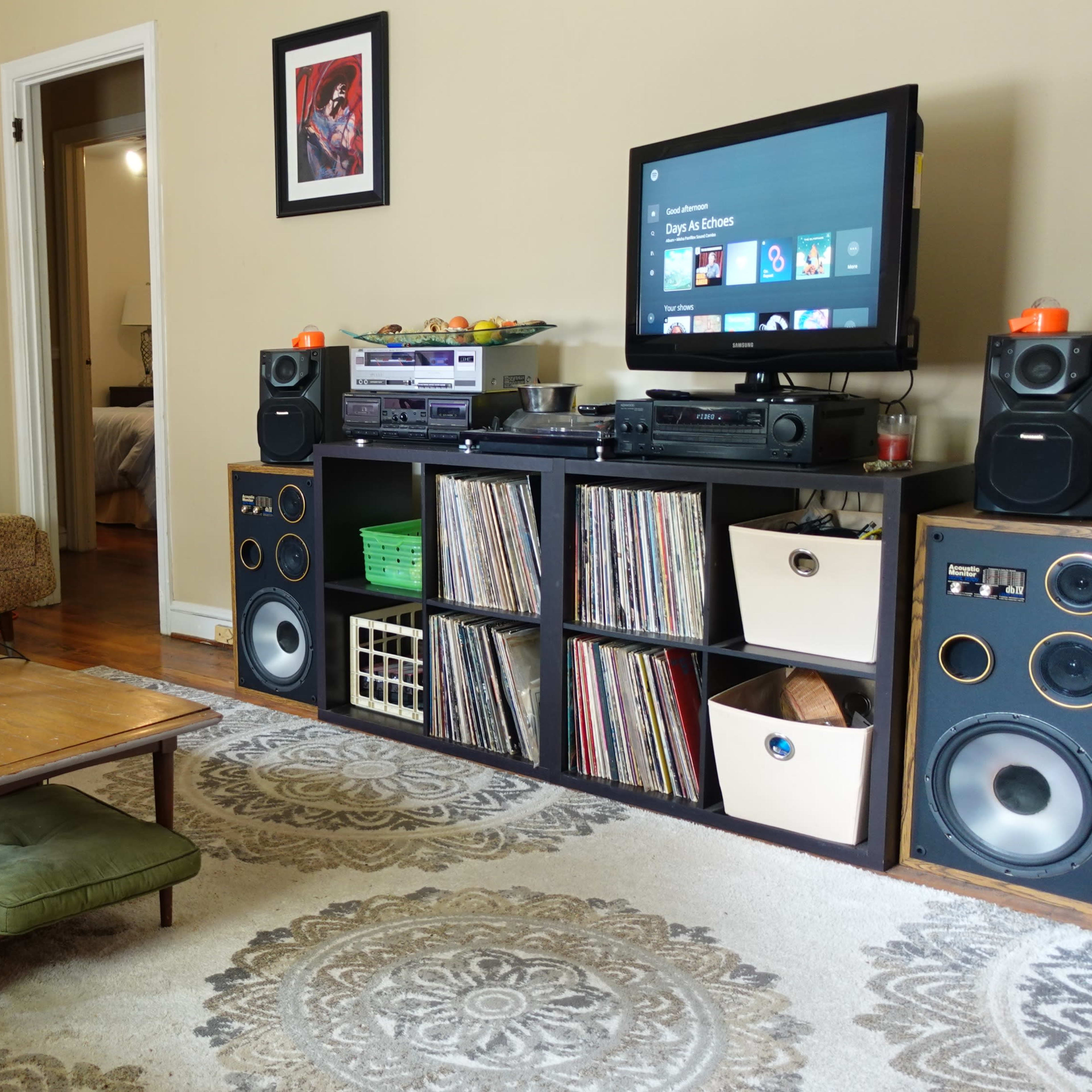 A living room features a muted color scheme, with a couch, a coffee table, a microphone on a stand, a television, and shelves holding vinyl records and audio equipment.