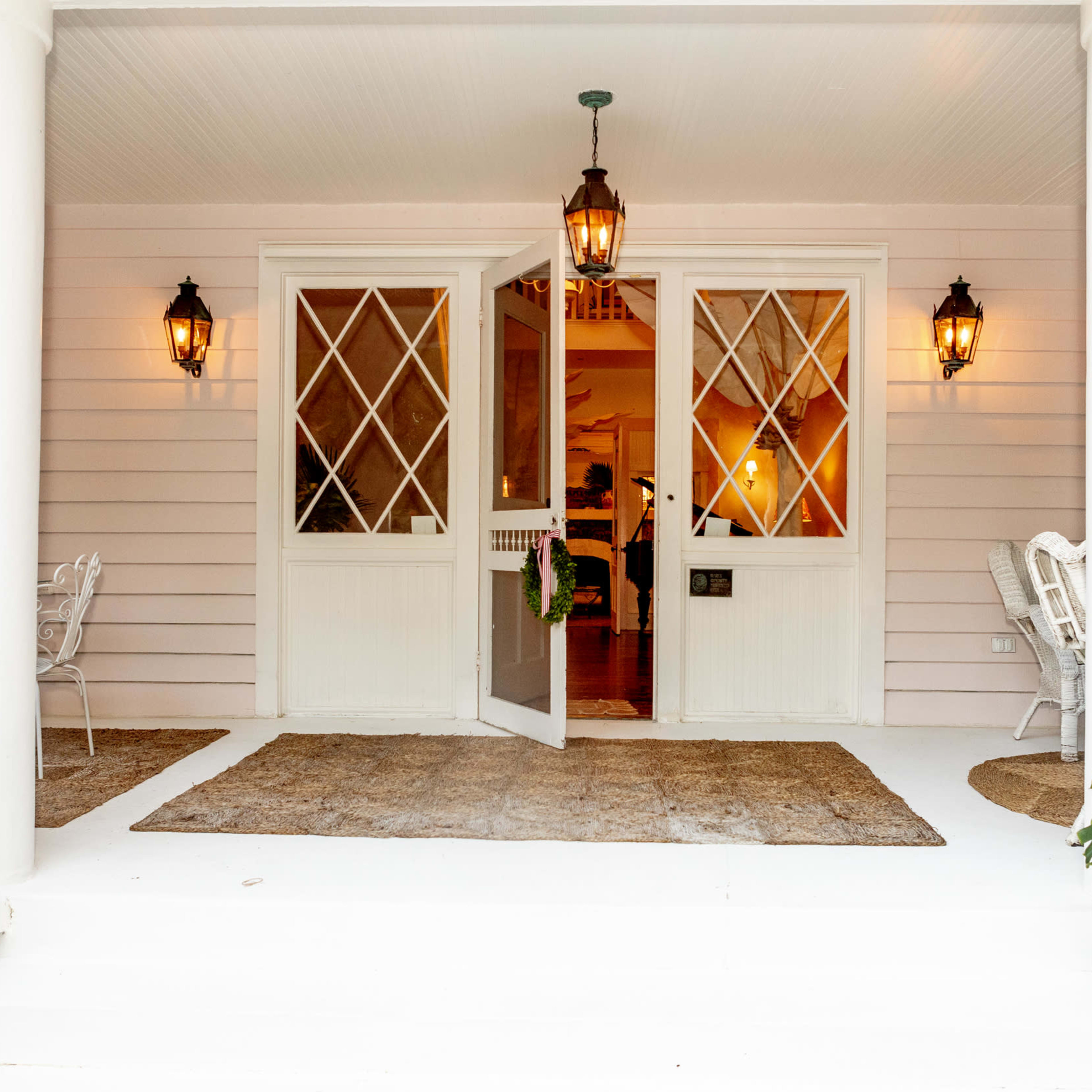 A welcoming entryway with open double doors, two lanterns flanking the entrance, and outdoor seating arranged on a porch.