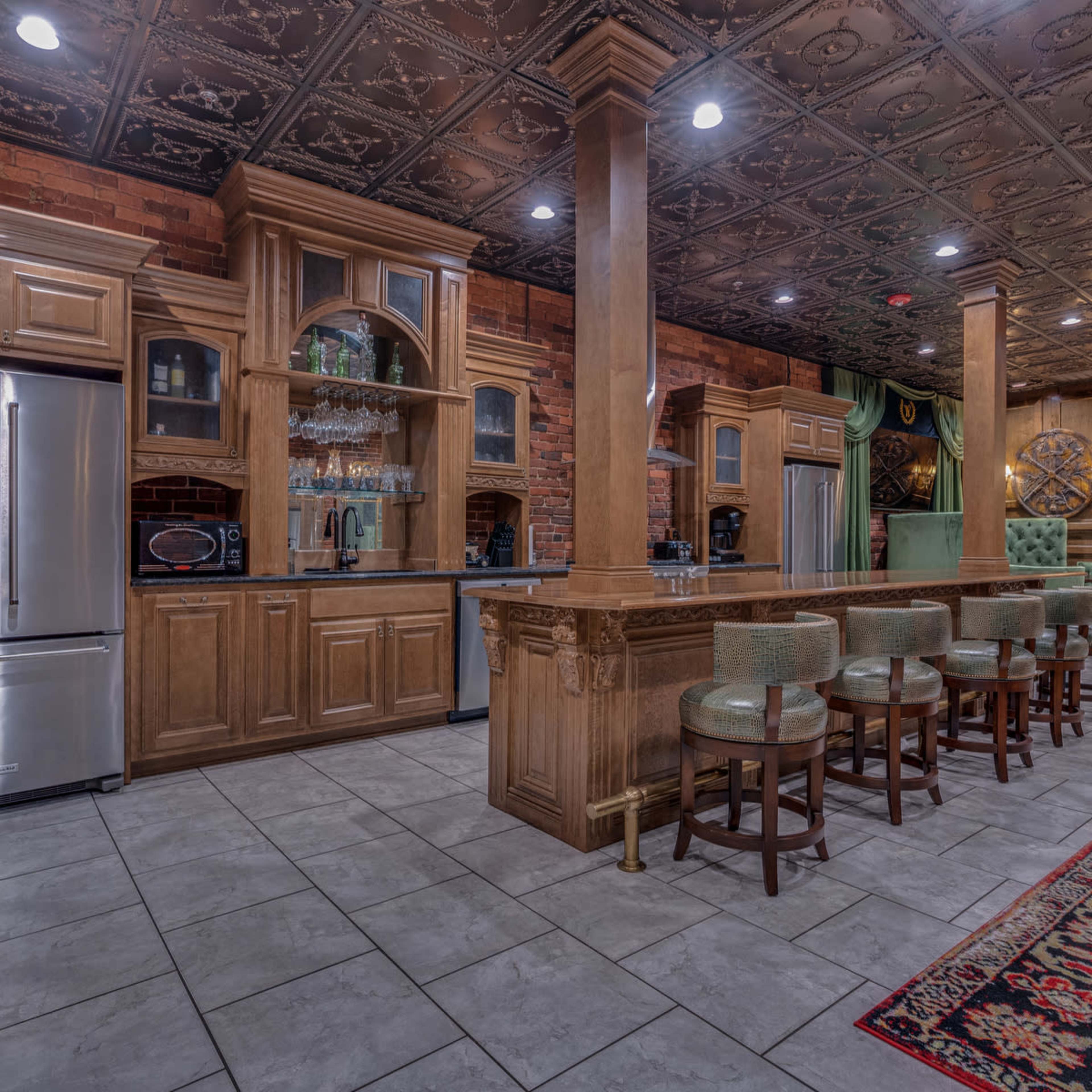 A spacious kitchen with wooden cabinetry, stainless steel appliances, a bar with stools, and decorative ceiling tiles.