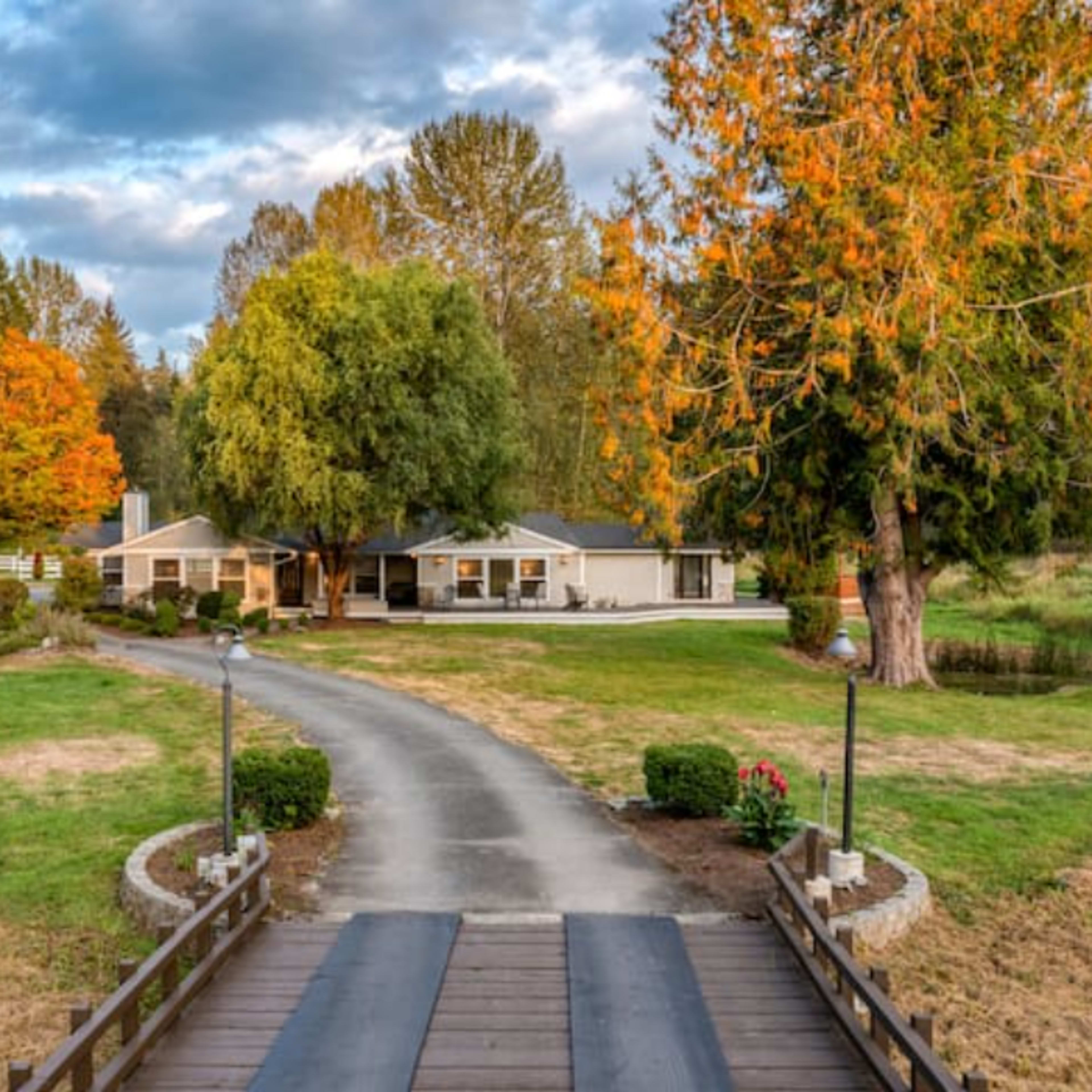 A long driveway leads to a spacious home surrounded by trees and a grassy area.