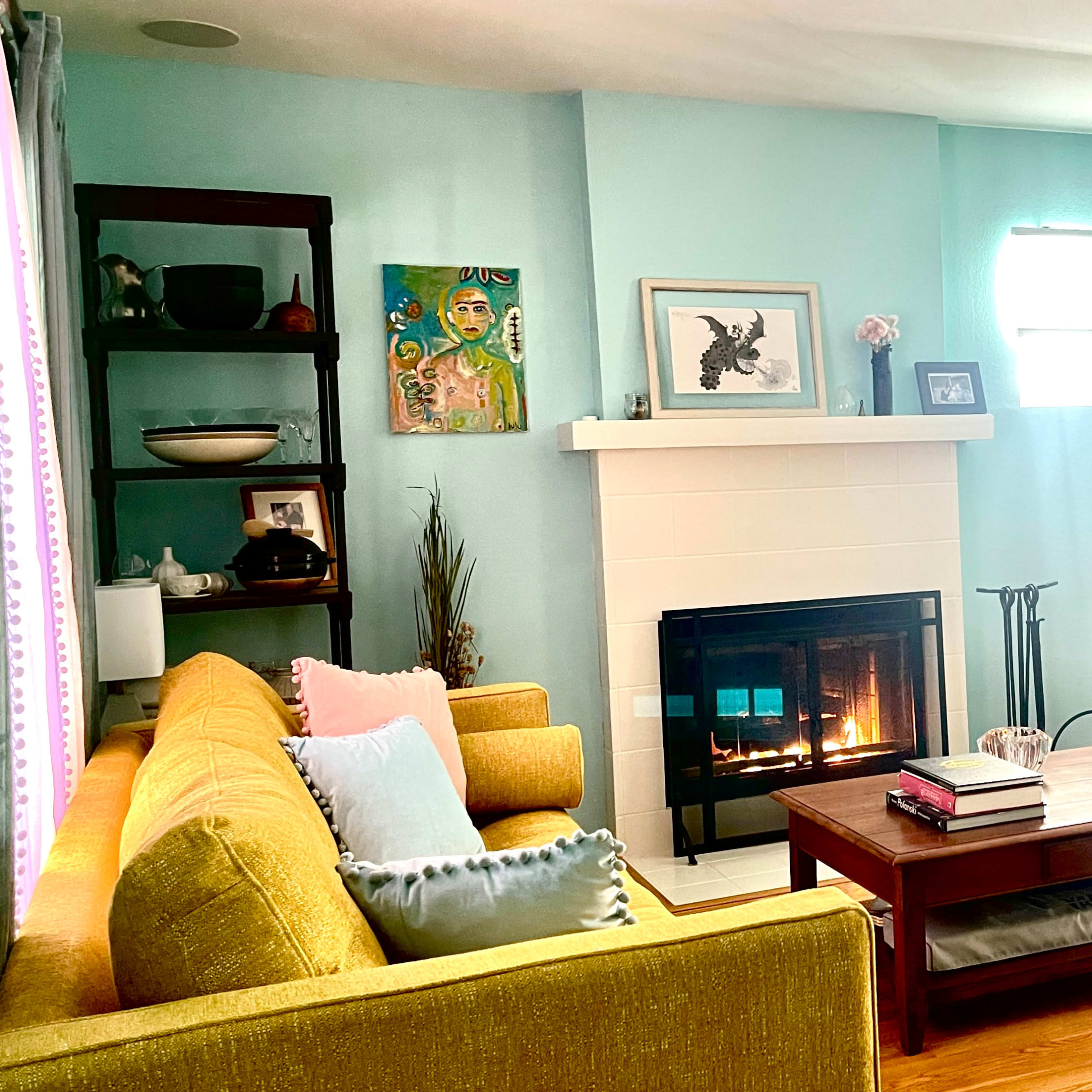 A brightly lit living room features a yellow sofa, a gray armchair, a fireplace, and a large TV on an entertainment unit.