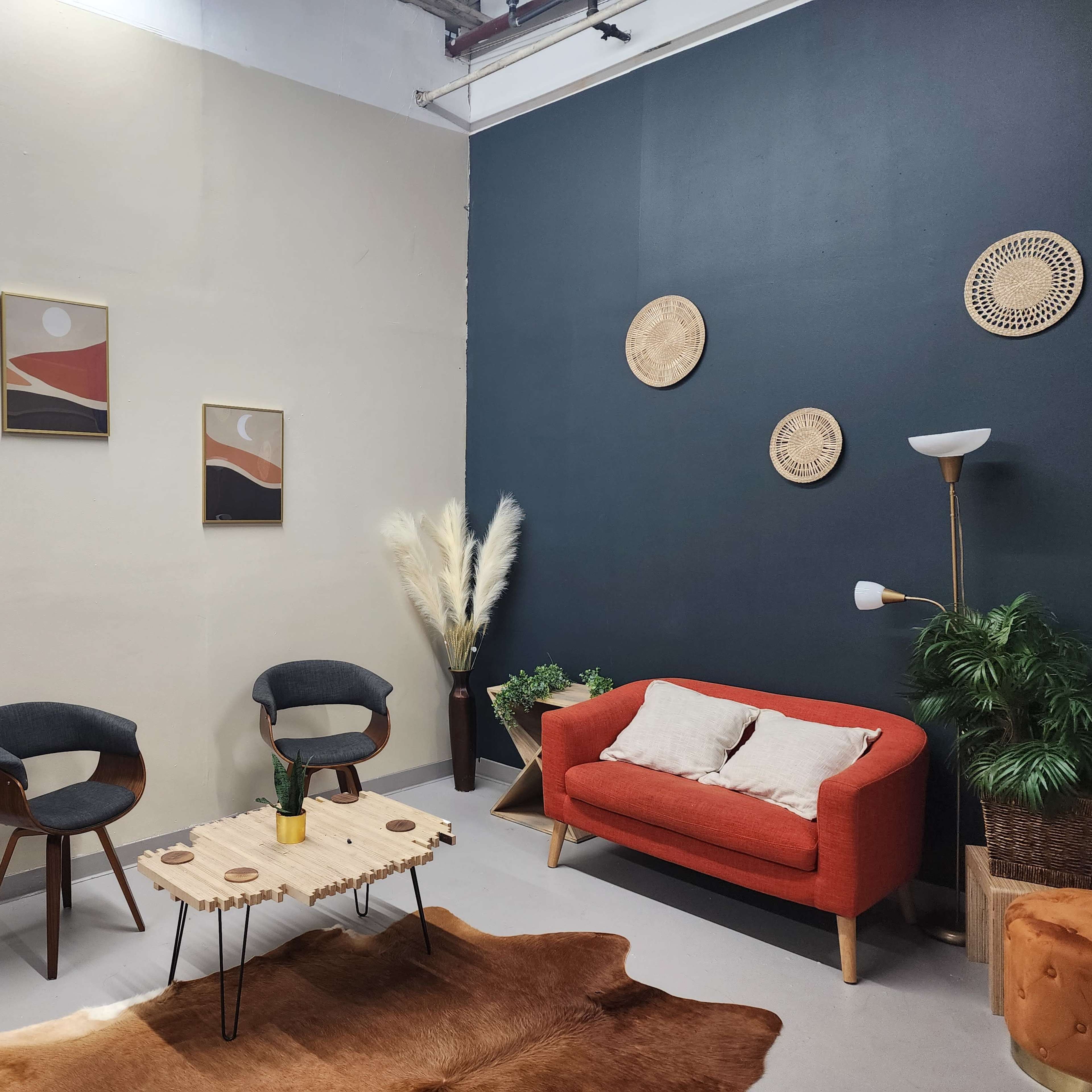 A modern lounge area with an orange sofa, two gray chairs, a wooden coffee table, and decor items including wall art and plants.