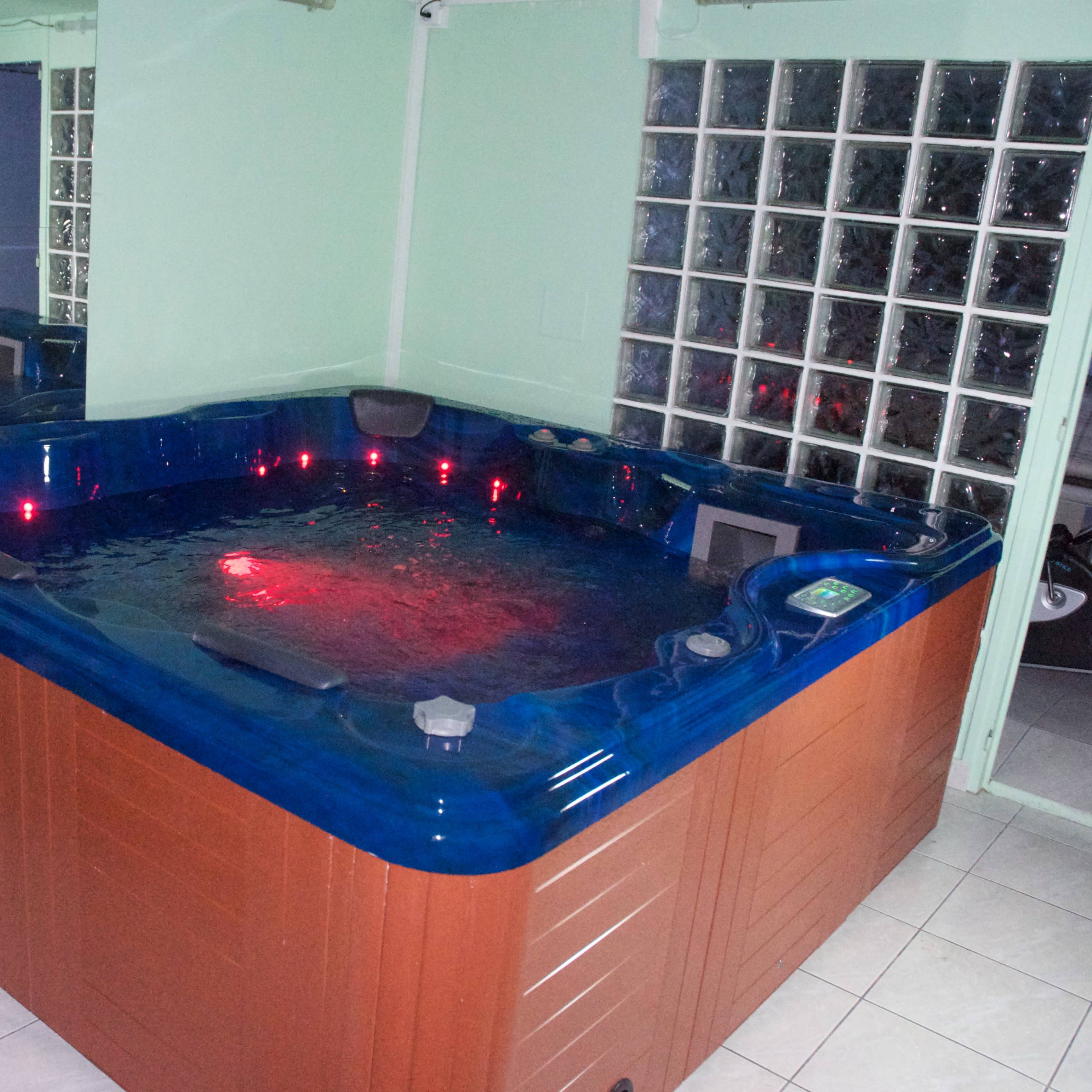 A hot tub with blue water and red lights, located in a tiled room with glass block windows.