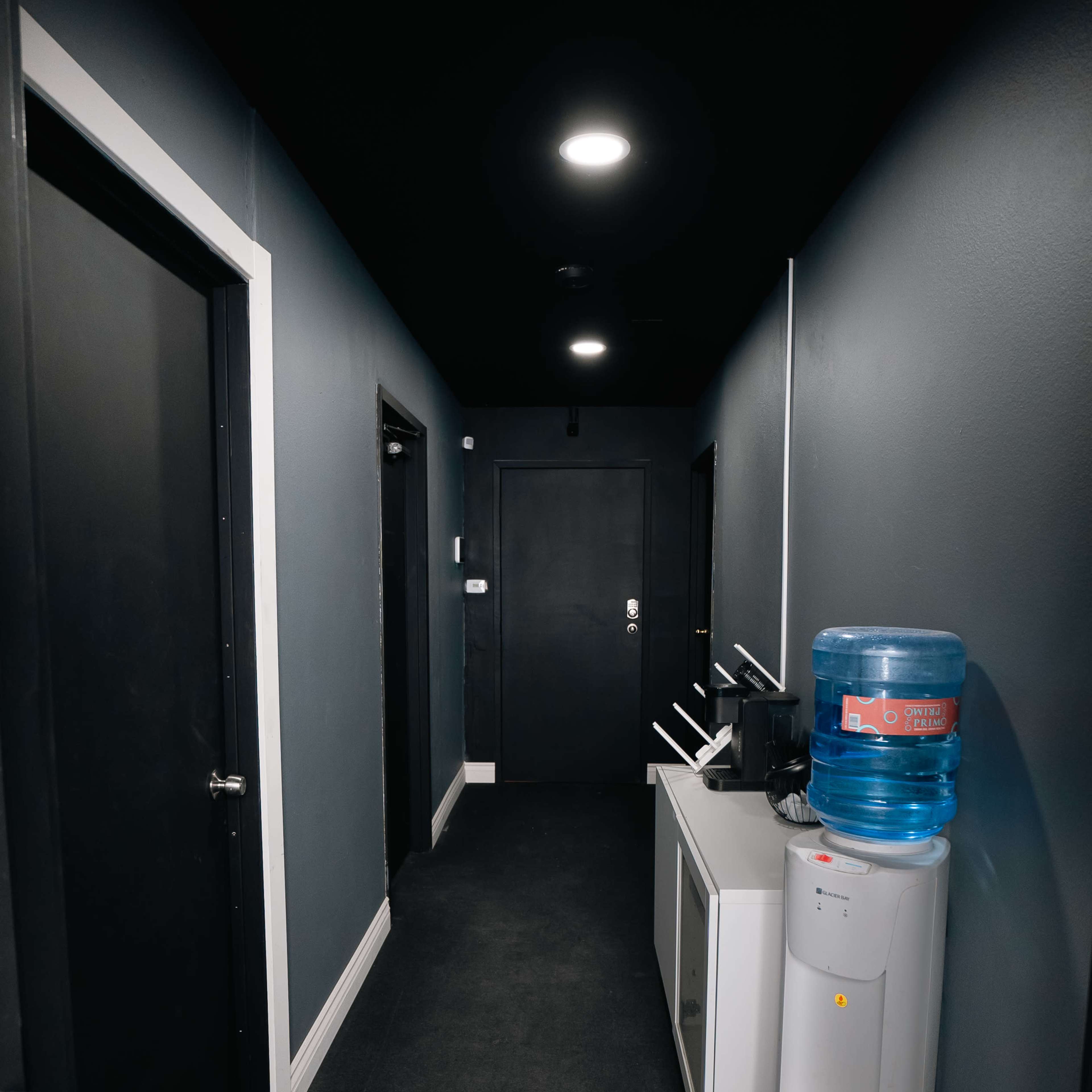 A narrow hallway features dark doors on either side, with a water cooler and a cabinet against one wall.