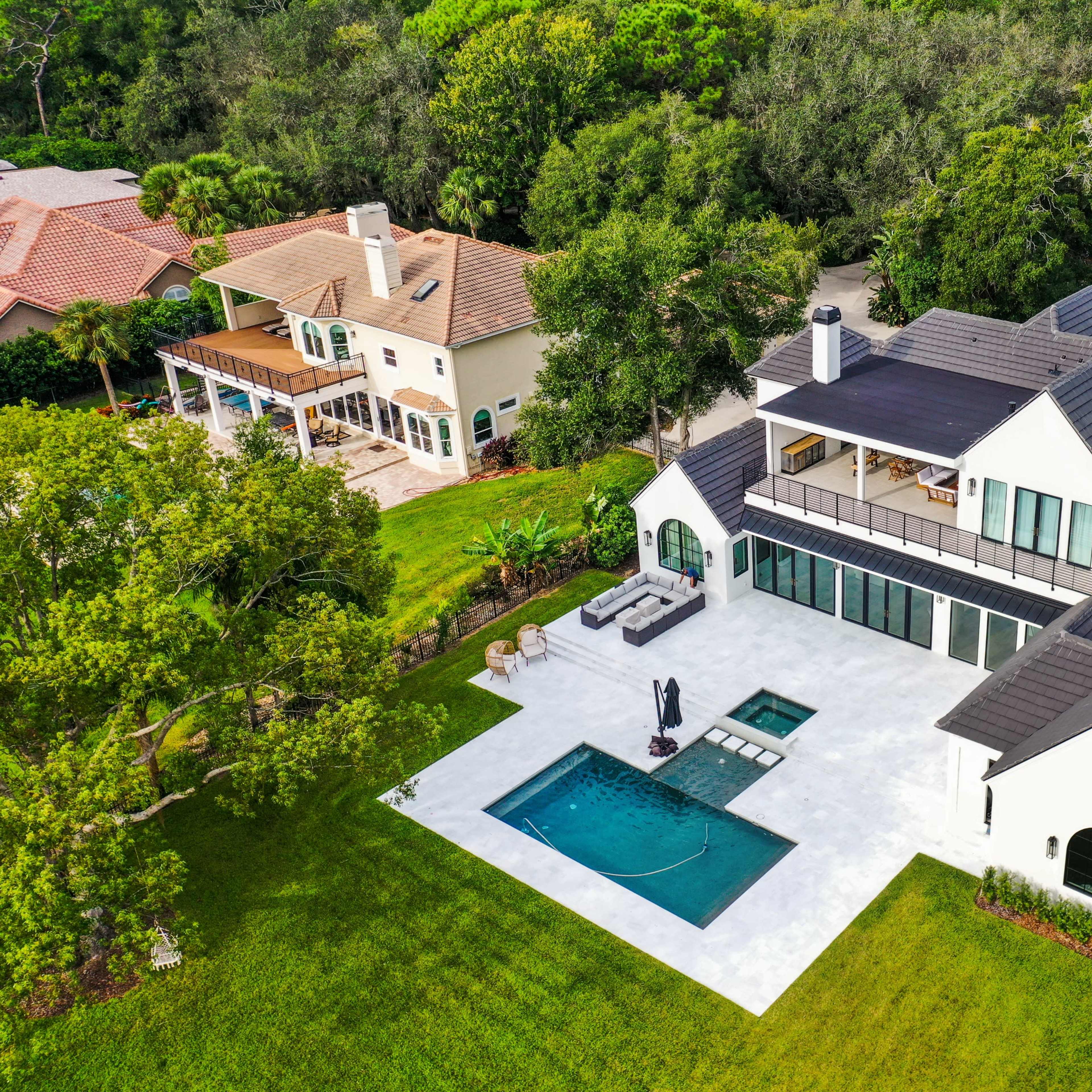 A modern two-story house with a pool and outdoor seating area surrounded by greenery.