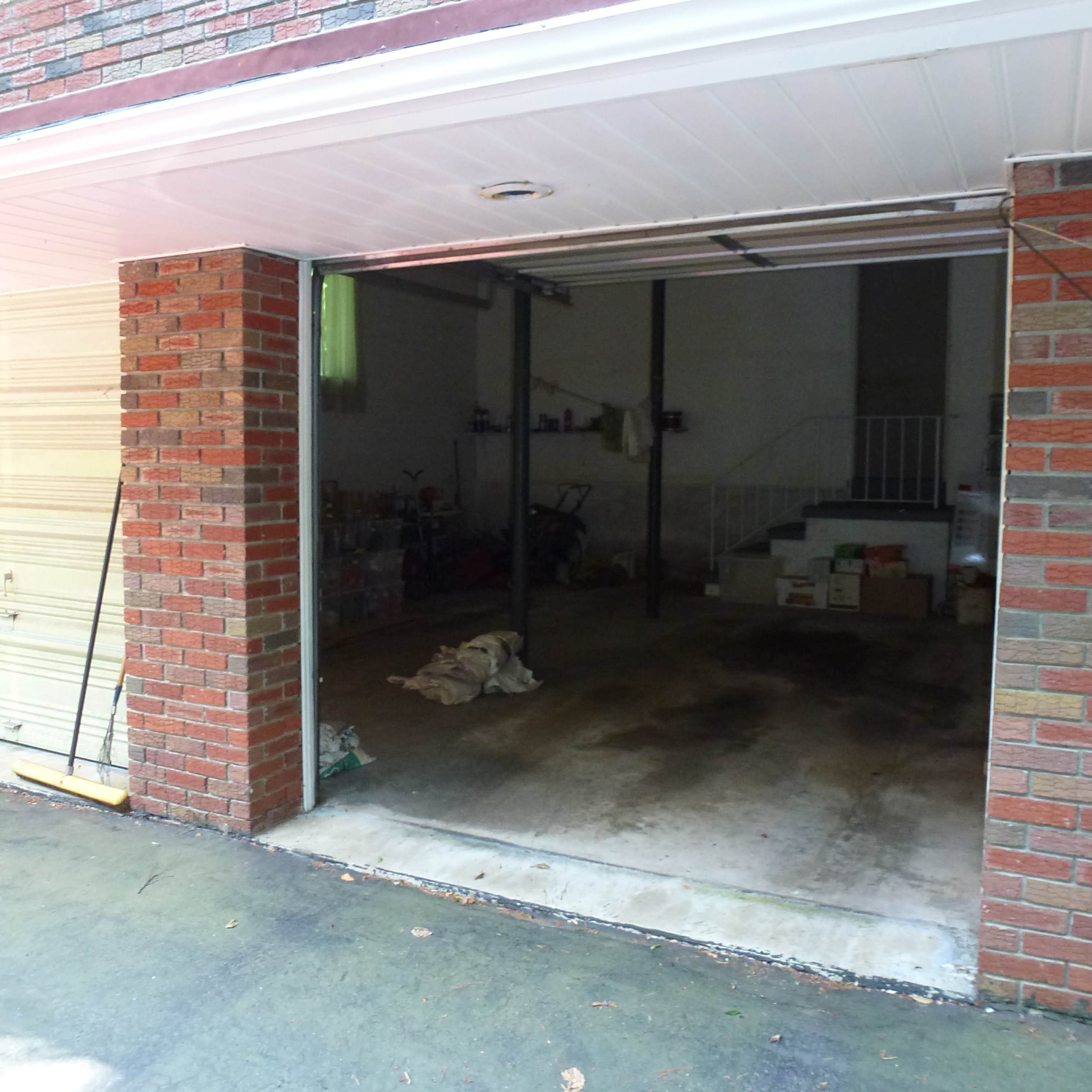 A two-car garage with an open door, revealing a concrete floor and scattered items in the background.