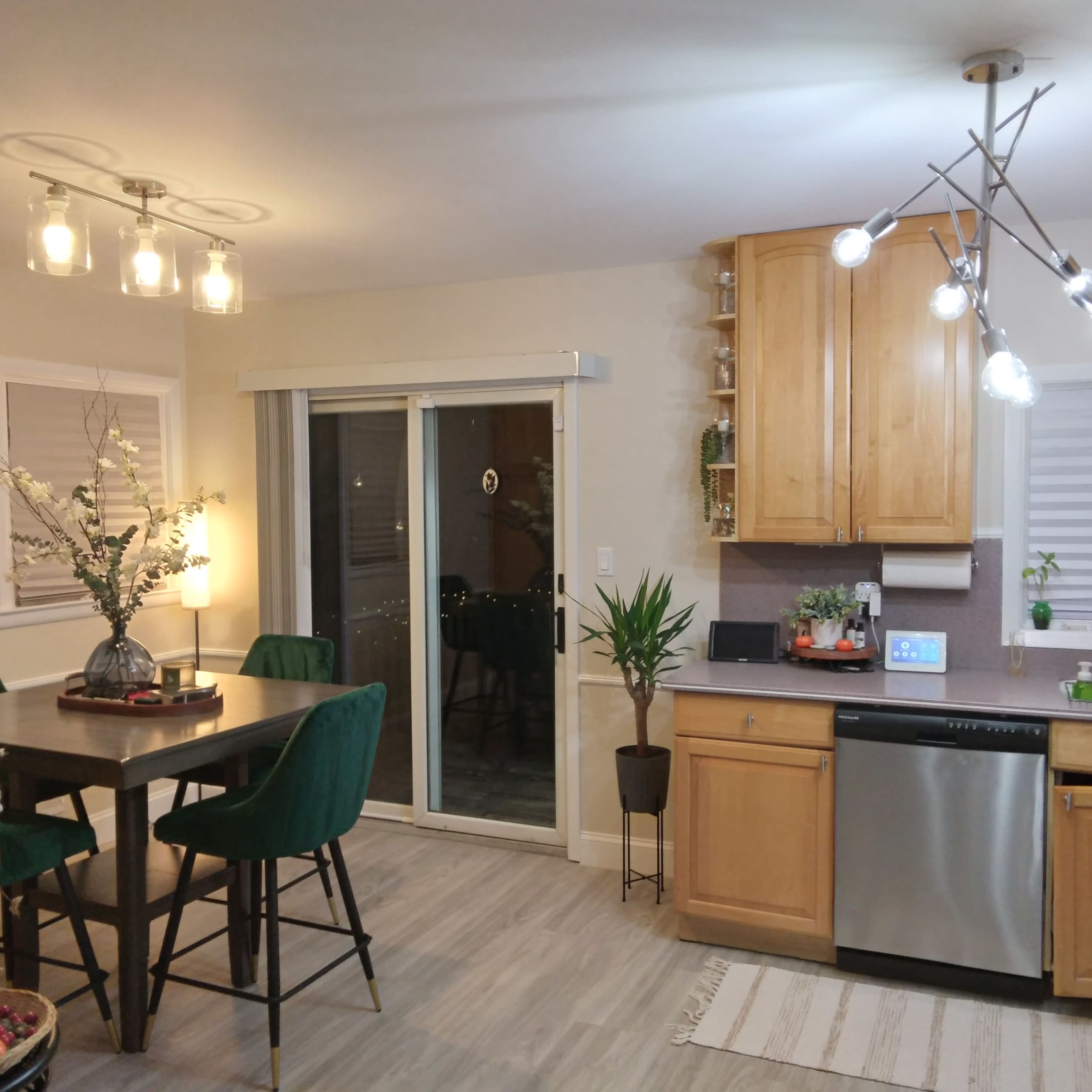 A modern kitchen and dining area featuring wooden cabinetry, a large table with green chairs, and large sliding glass doors leading to a patio.