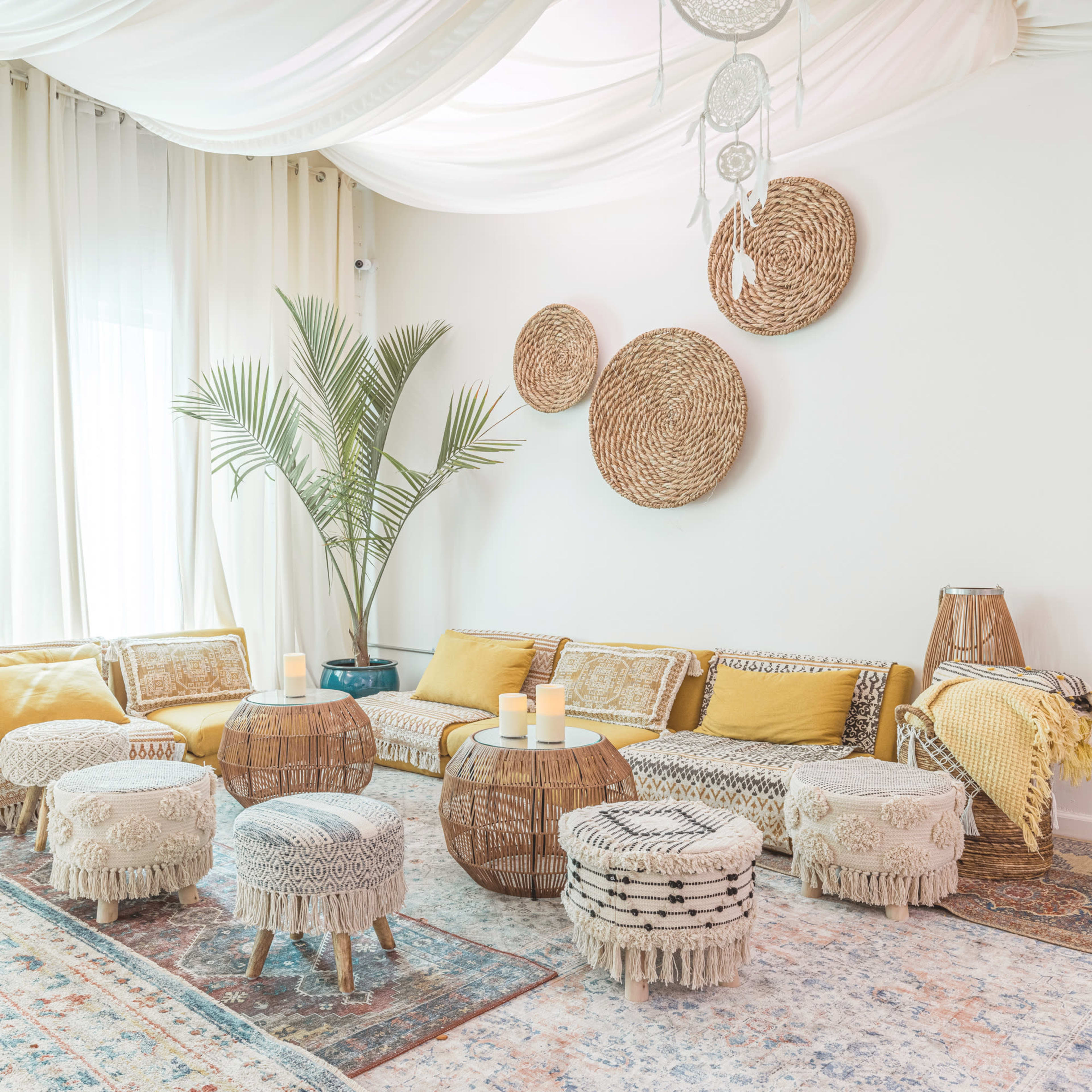 A cozy living room with a large, U-shaped sofa adorned with yellow and neutral cushions, surrounded by woven furniture, decorative rugs, and illuminated candles.