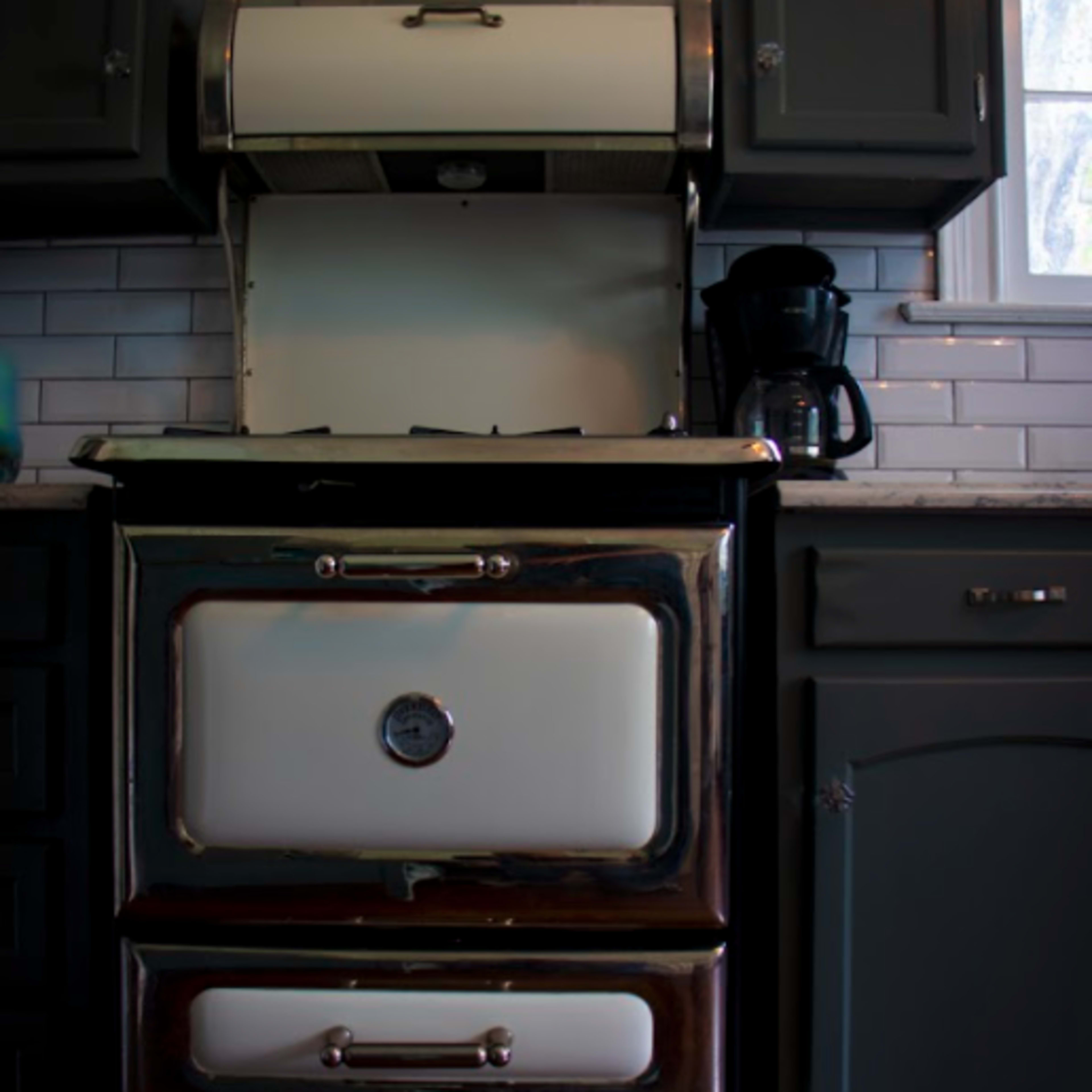 A vintage-style stove with a polished chrome exterior and white enamel accents, set against a backdrop of gray kitchen cabinets and a subway tile backsplash.