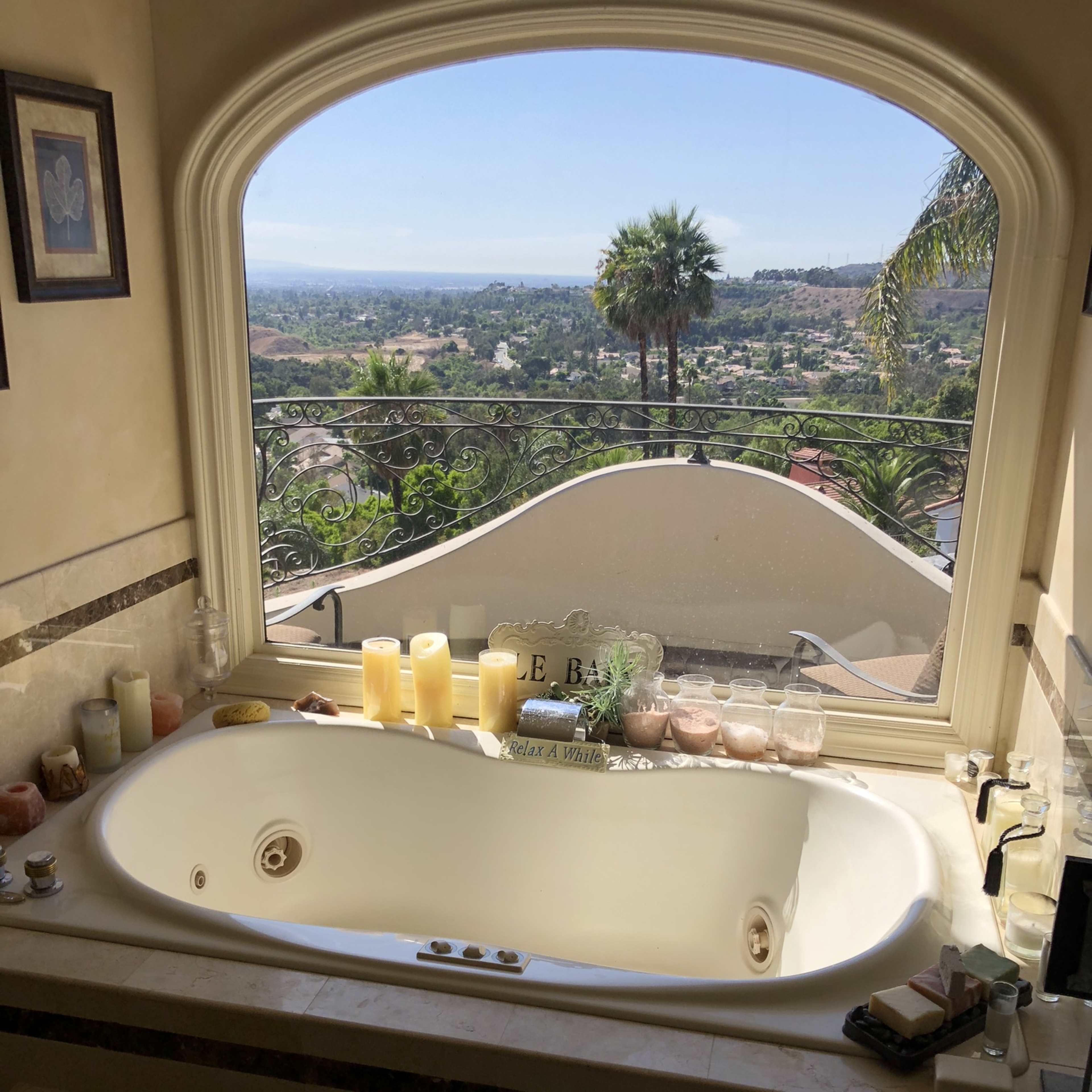 A large jacuzzi tub is positioned beneath a wide arched window that offers a view of a landscape filled with trees and distant hills.