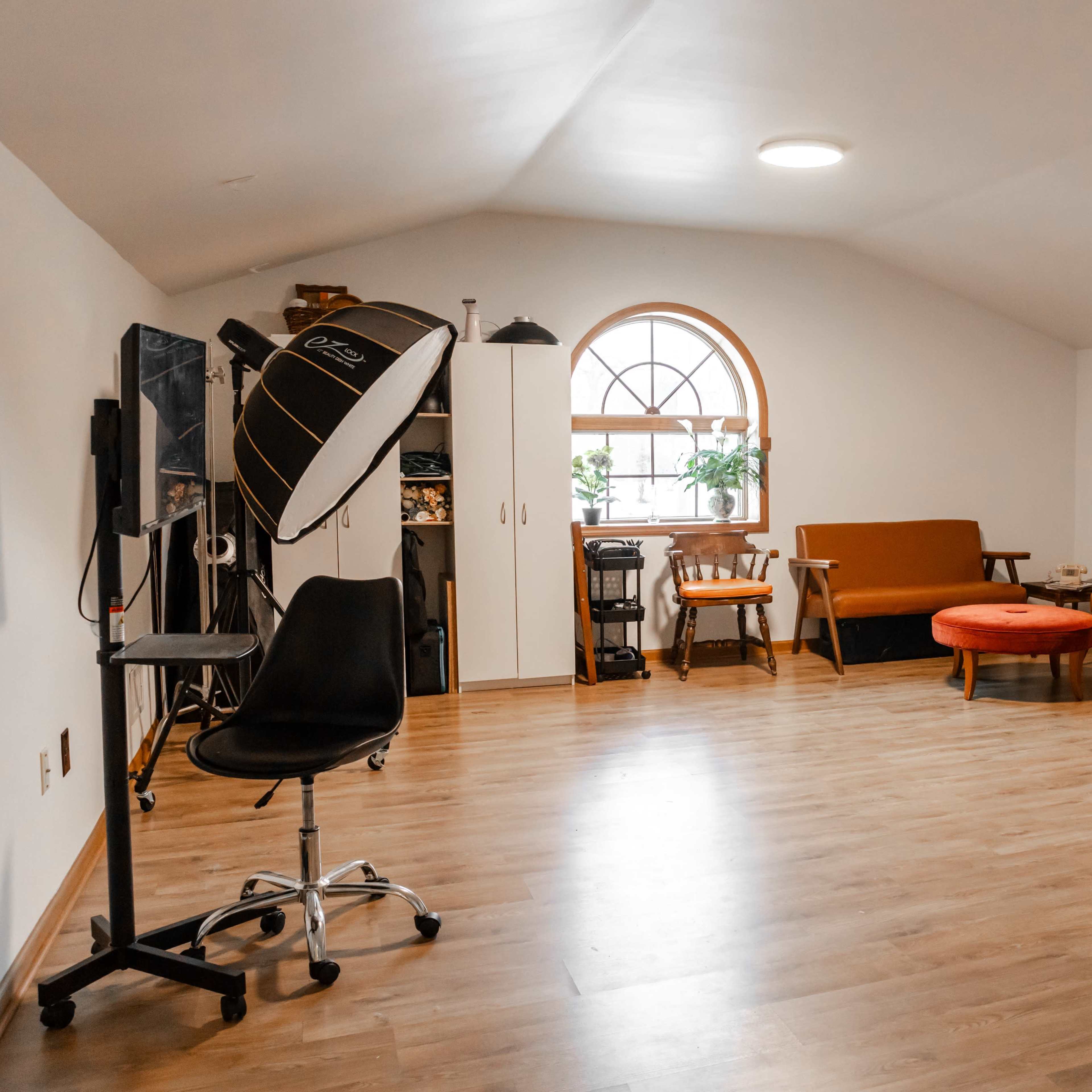 A spacious, well-lit room featuring a mix of furniture, including a sofa, chairs, a table, and a backdrop for photography.
