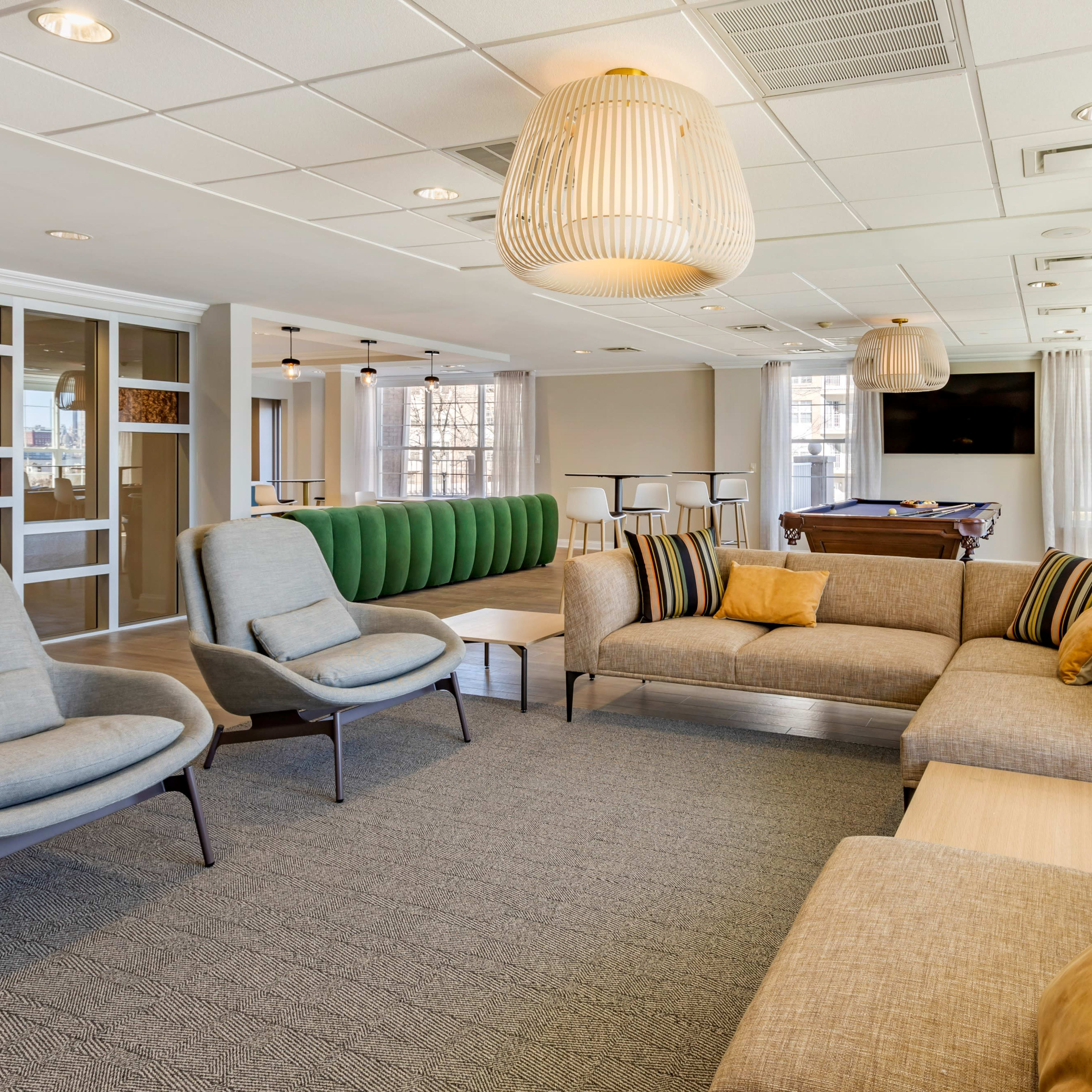 A modern lounge area with a combination of comfortable seating, a pool table, and large windows allowing natural light to fill the space.