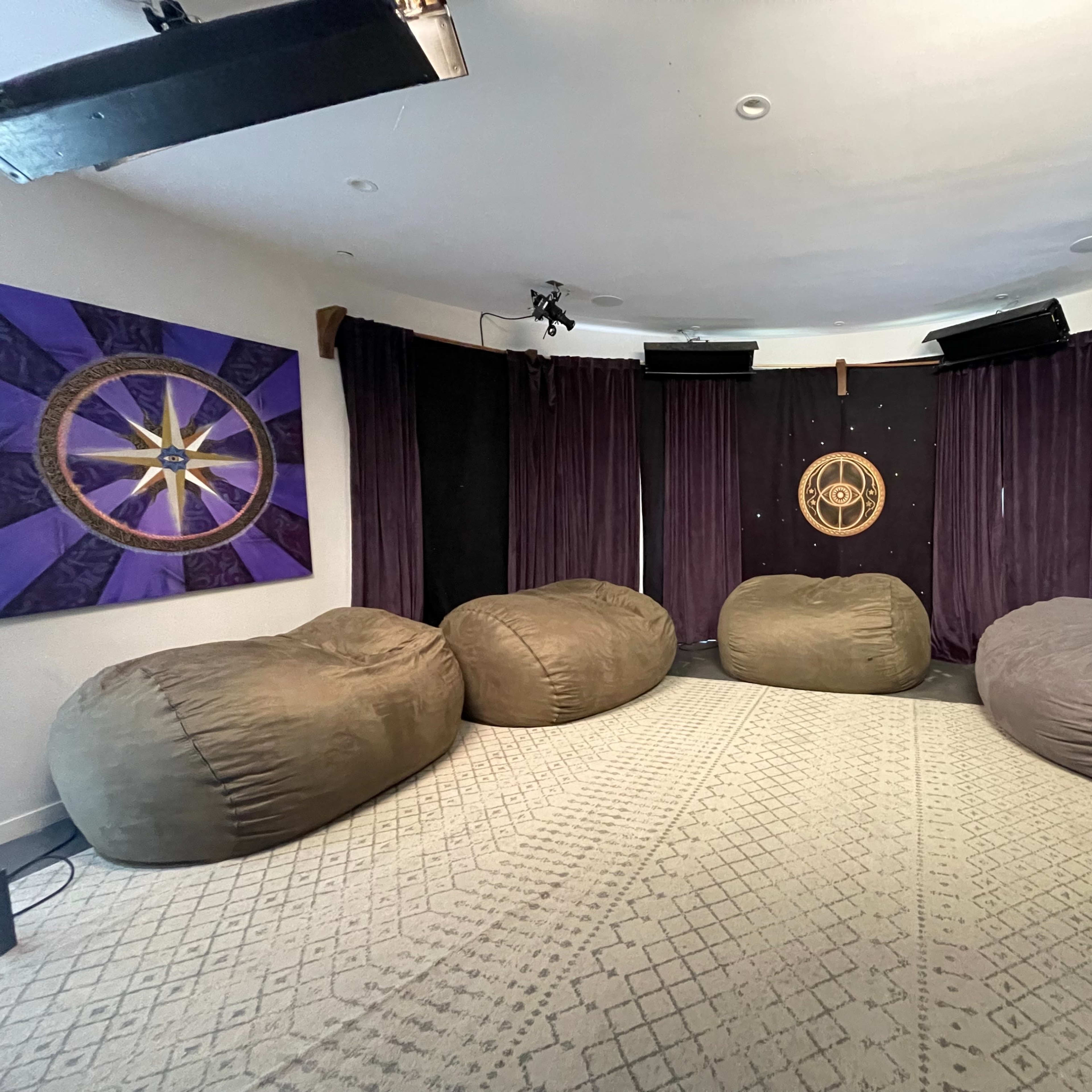A cozy room with bean bag chairs arranged in a semicircle, surrounded by dark curtains and adorned with a decorative wall hanging.