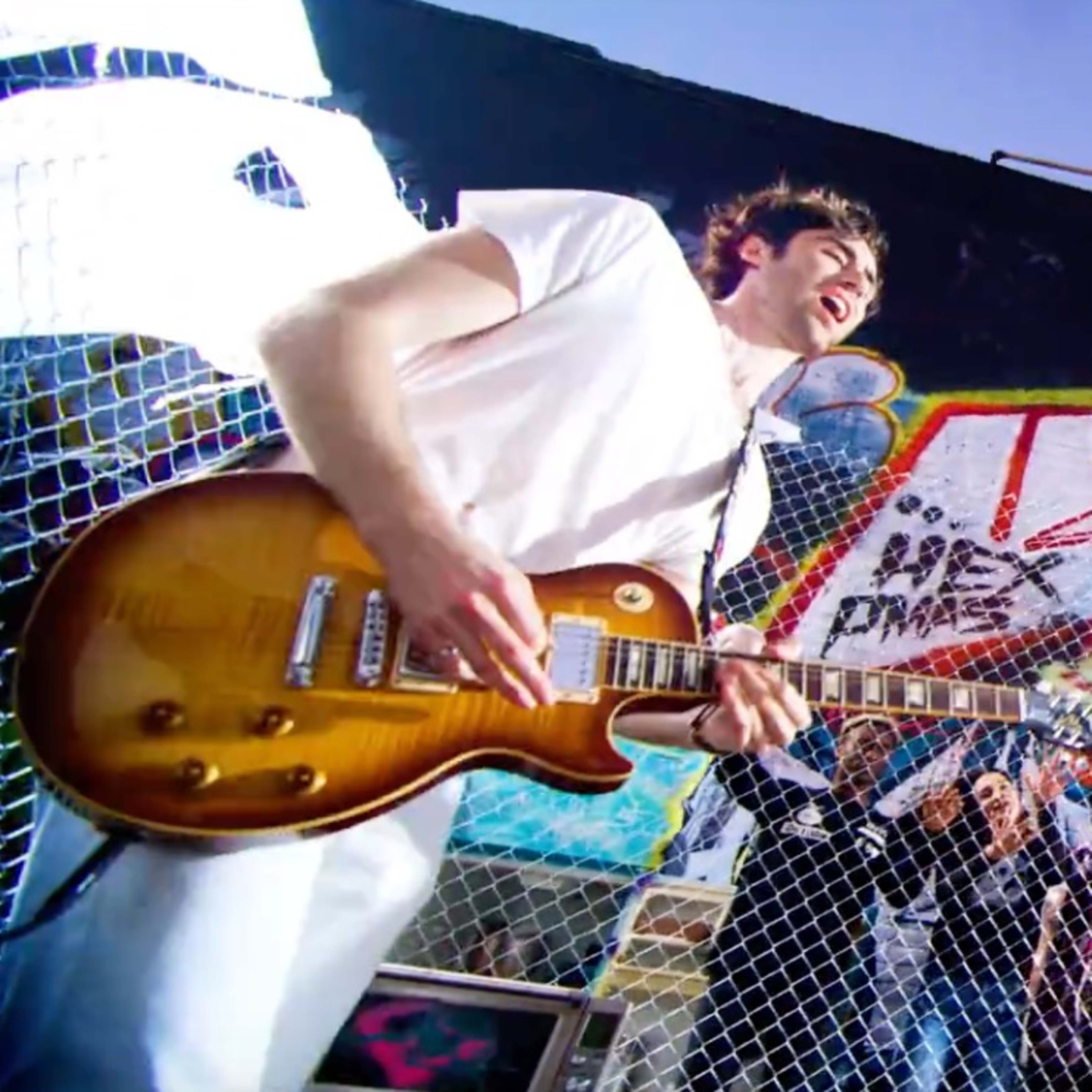 A band performs in front of a vibrant graffiti-covered wall while a crowd watches from behind a fence.