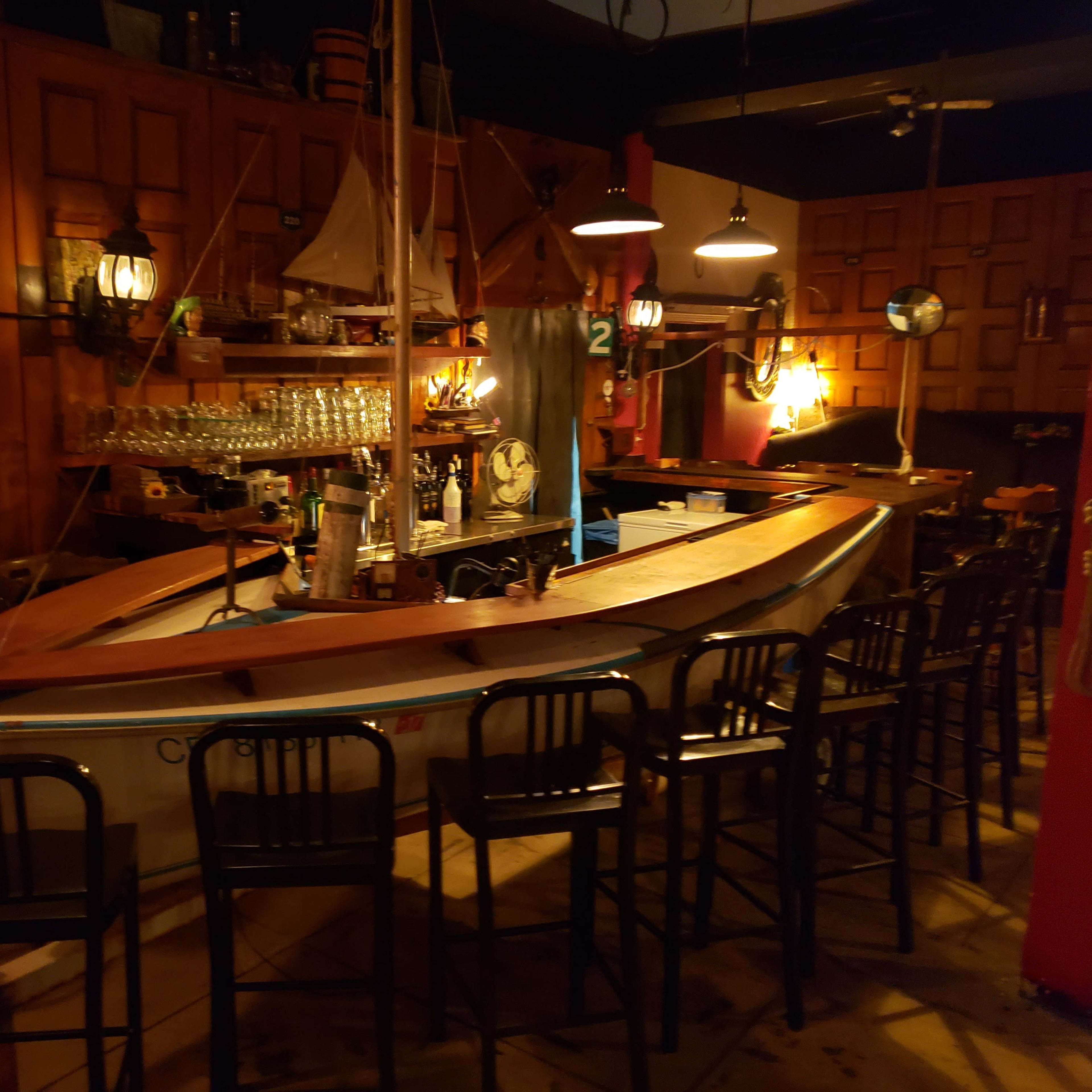 A wooden boat is set up as a bar centerpiece in a dimly lit room with high chairs and nautical decor.