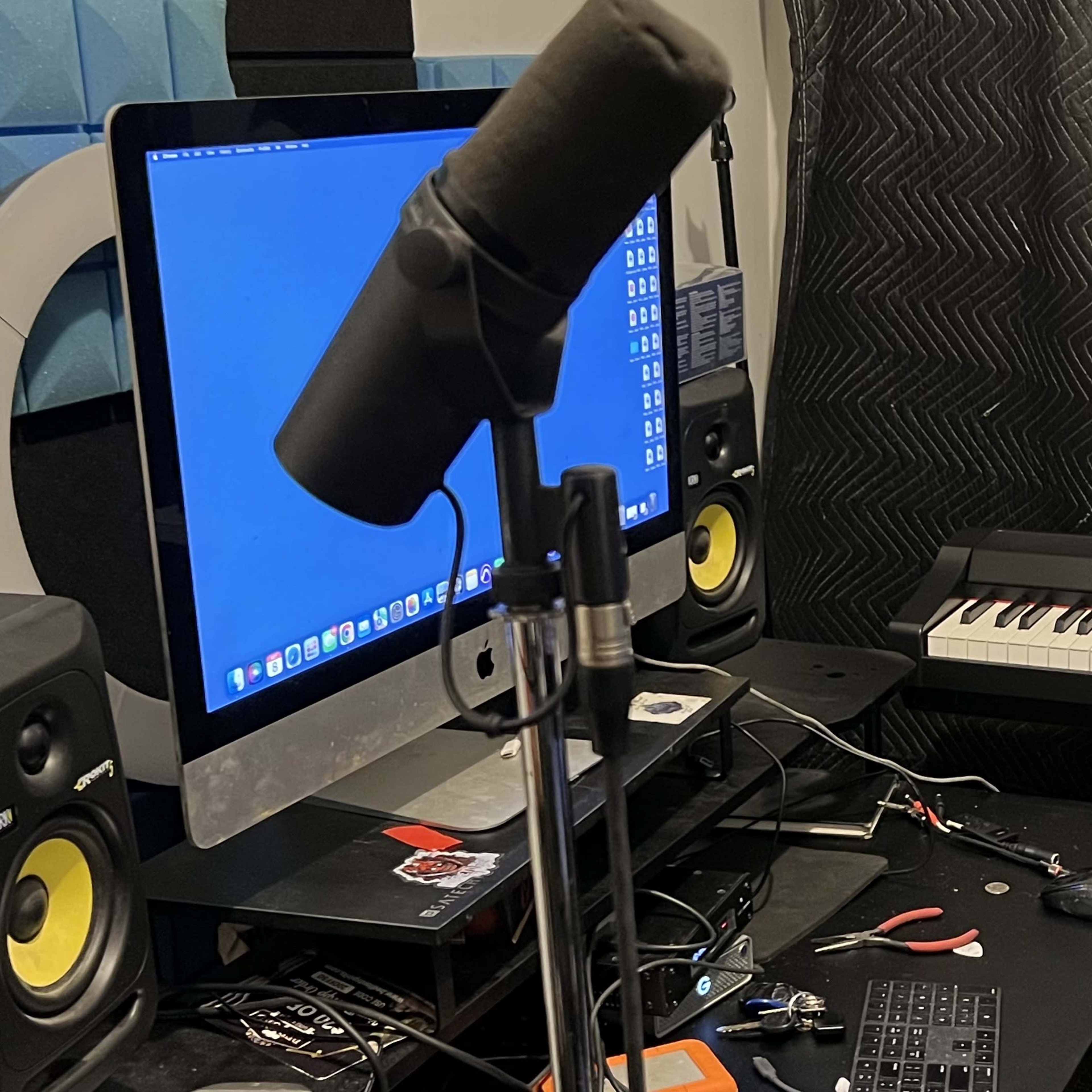A microphone stands in front of a computer and keyboard in a recording studio.