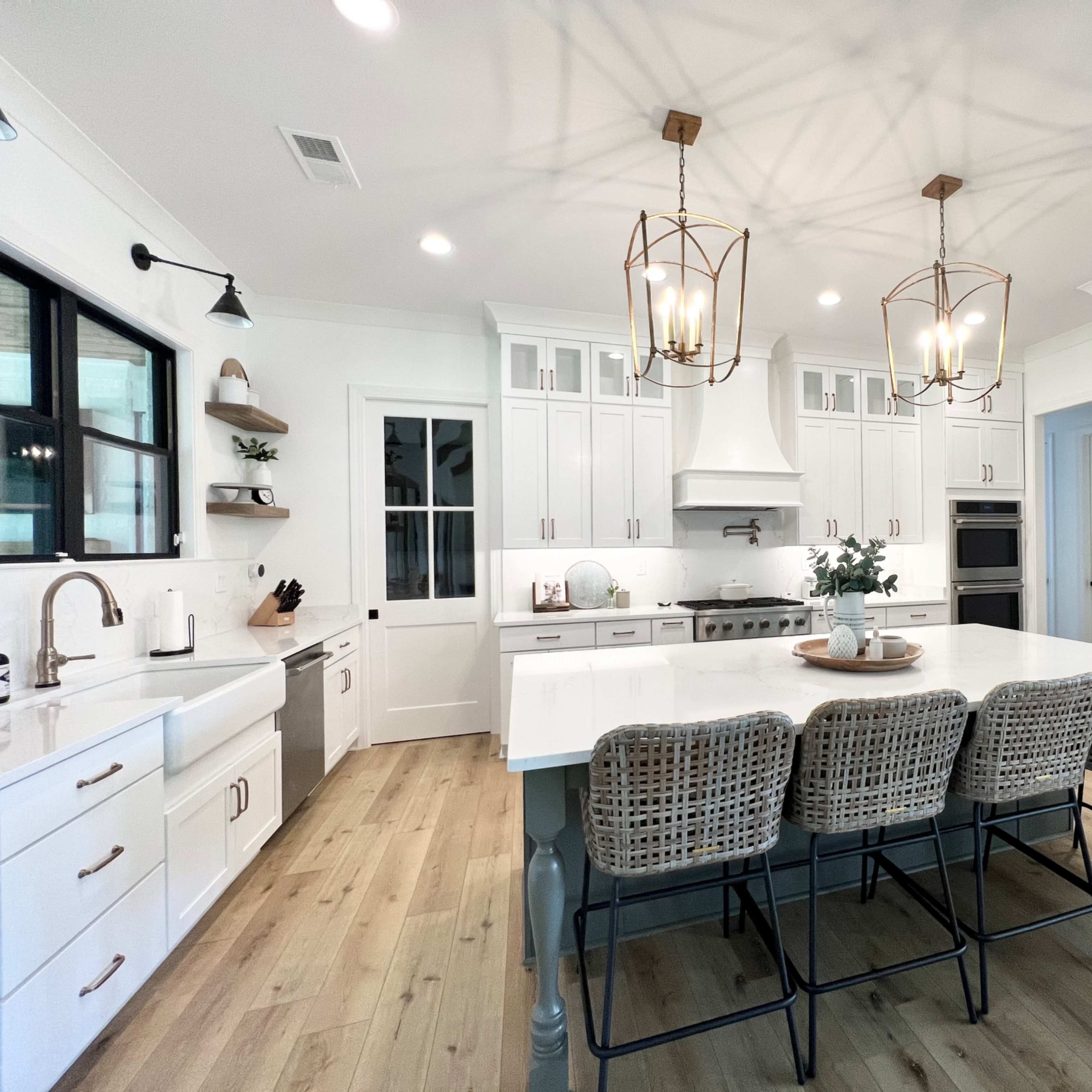 A modern kitchen featuring white cabinets, a large island with seating, stainless steel appliances, and pendant lighting.