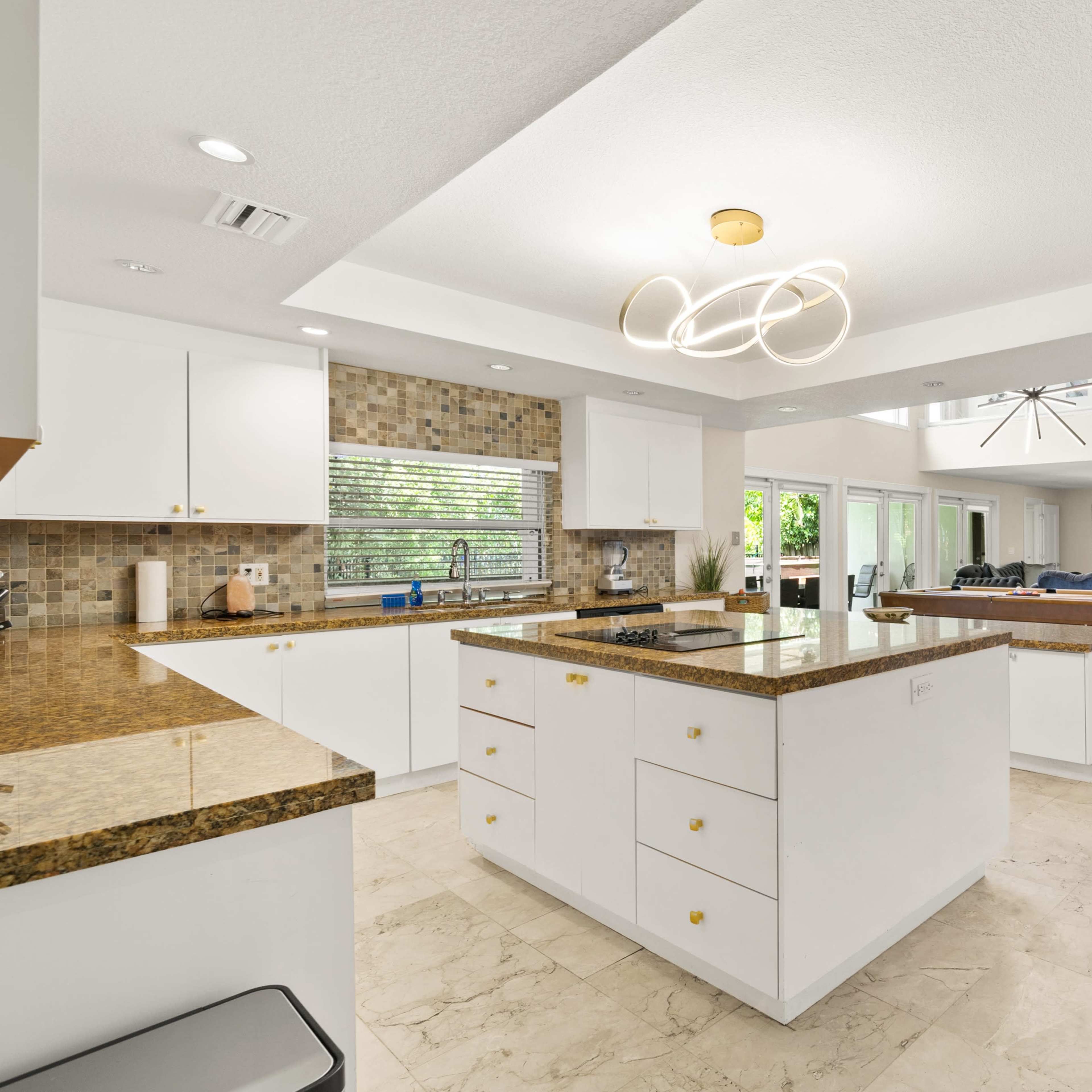 A modern kitchen features white cabinetry, granite countertops, and an open layout with a central island.