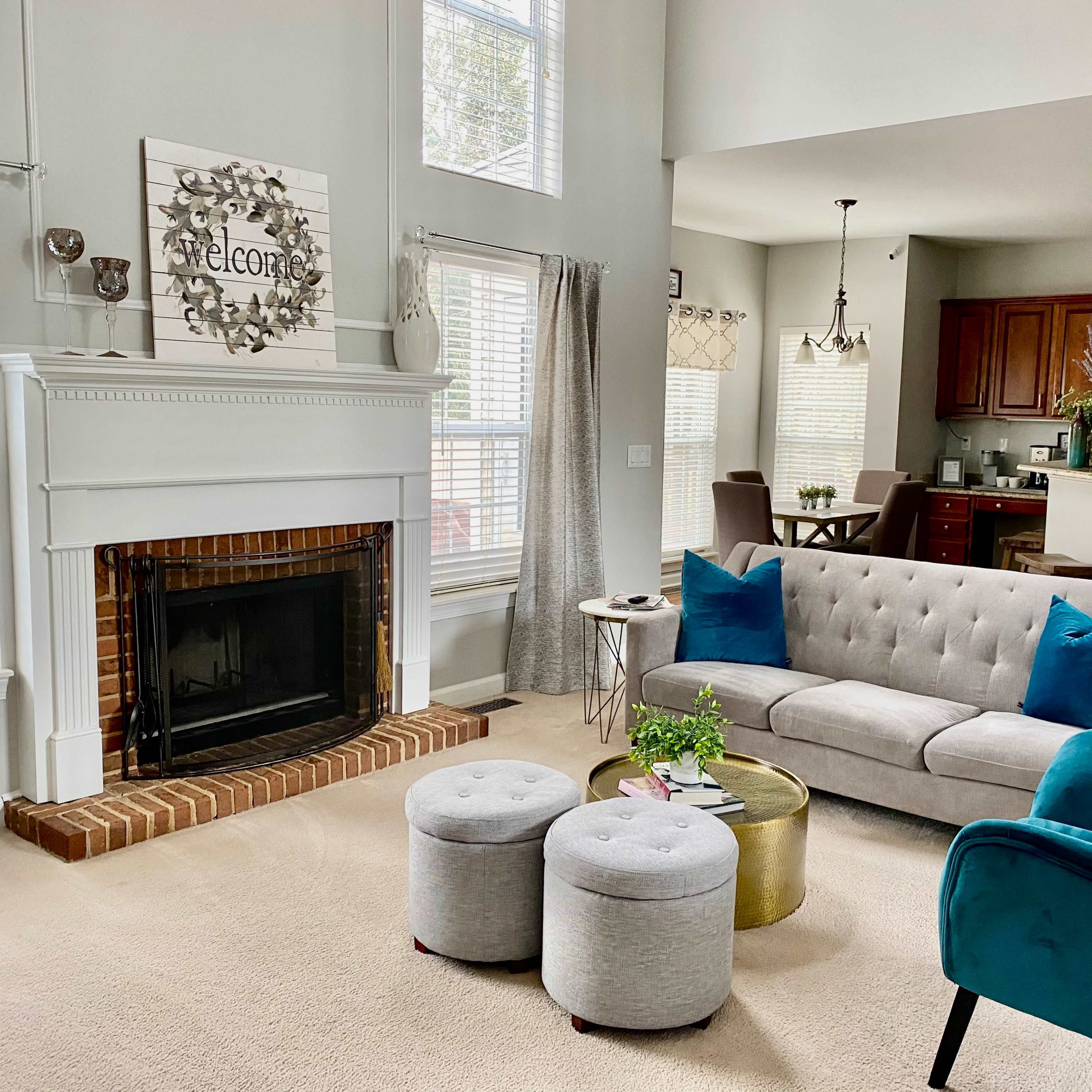 A modern living room features a gray sofa with blue pillows, a fireplace, and a small dining area visible in the background.