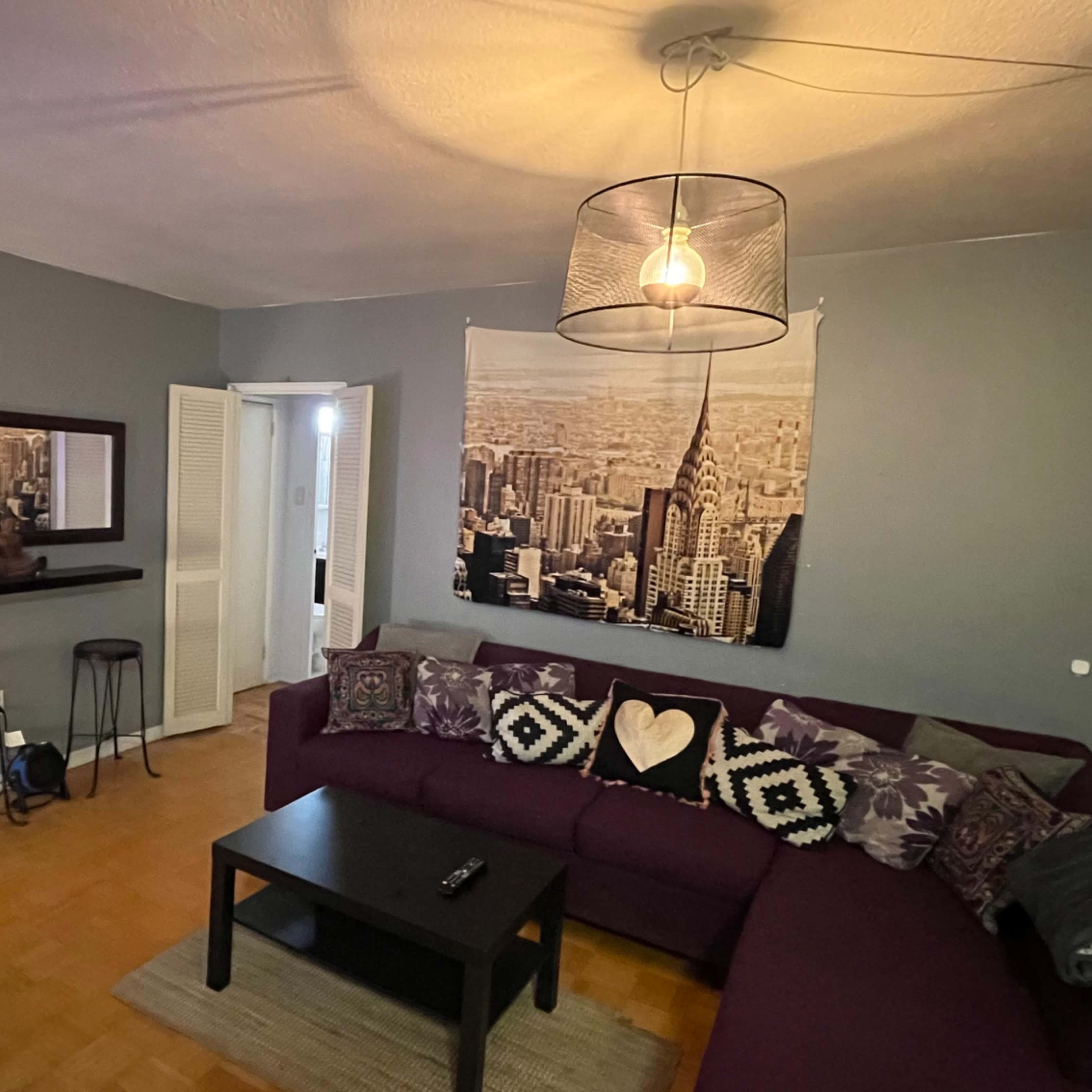 A cozy living room features a purple sectional sofa, a black coffee table, and a wall-mounted cityscape photograph.