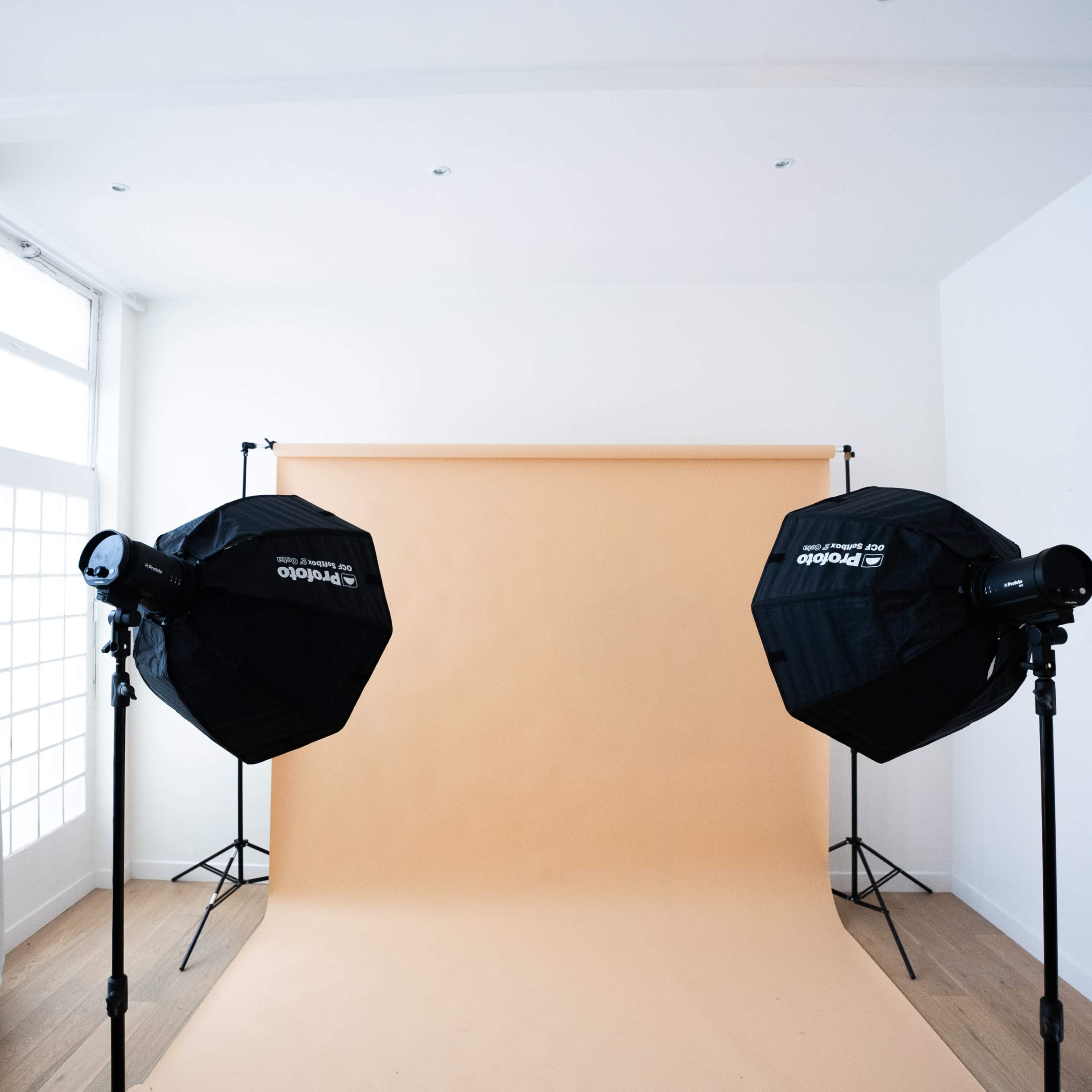 A photography studio with two softbox lights positioned in front of a plain orange backdrop.