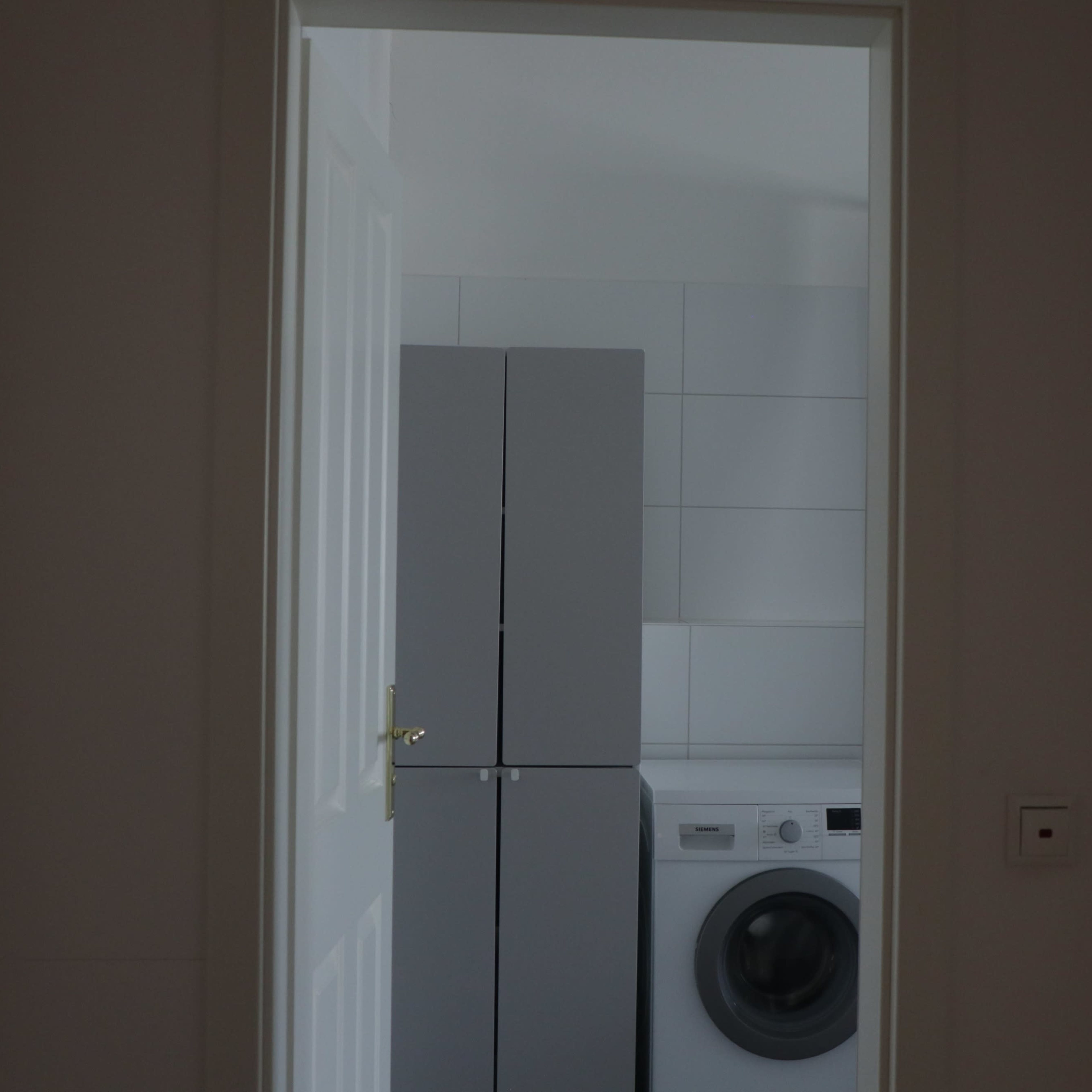 A laundry room is visible through an open door, featuring a washing machine and a tall gray cabinet.