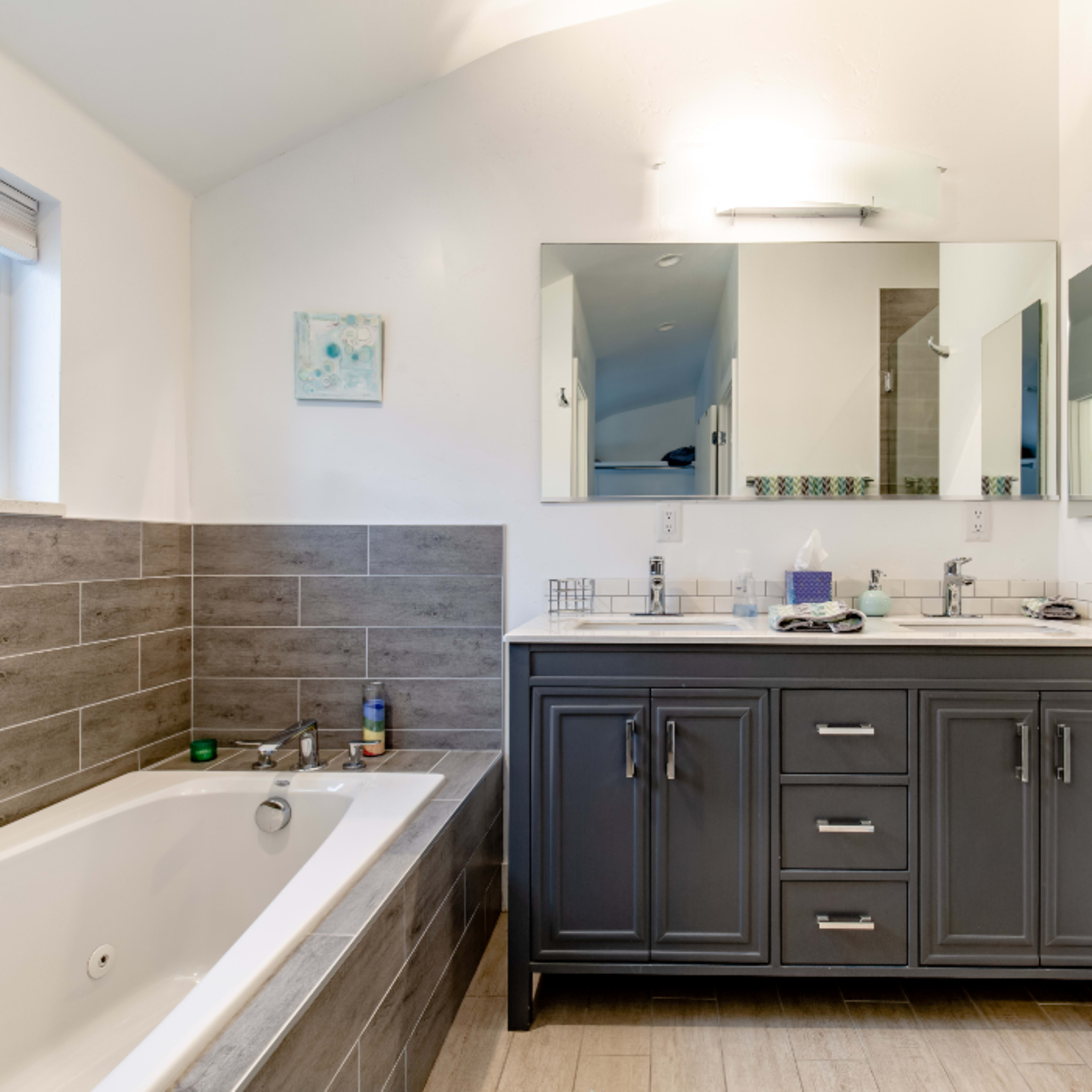 The bathroom features a double sink vanity with dark cabinetry, a large mirror, a freestanding bathtub, and tiled walls.