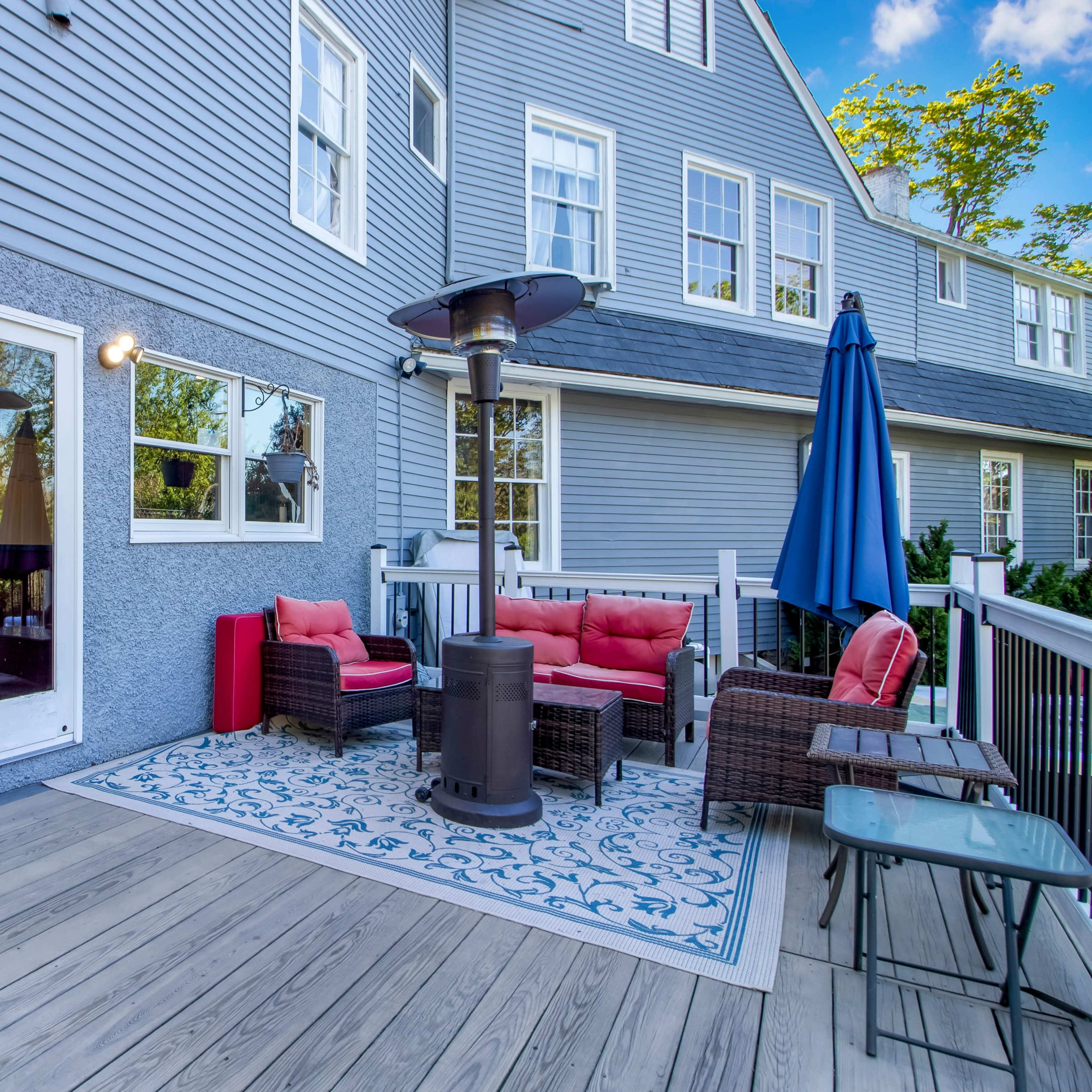 A deck area with patio furniture, a gas heater, and a blue umbrella against the backdrop of a gray house.