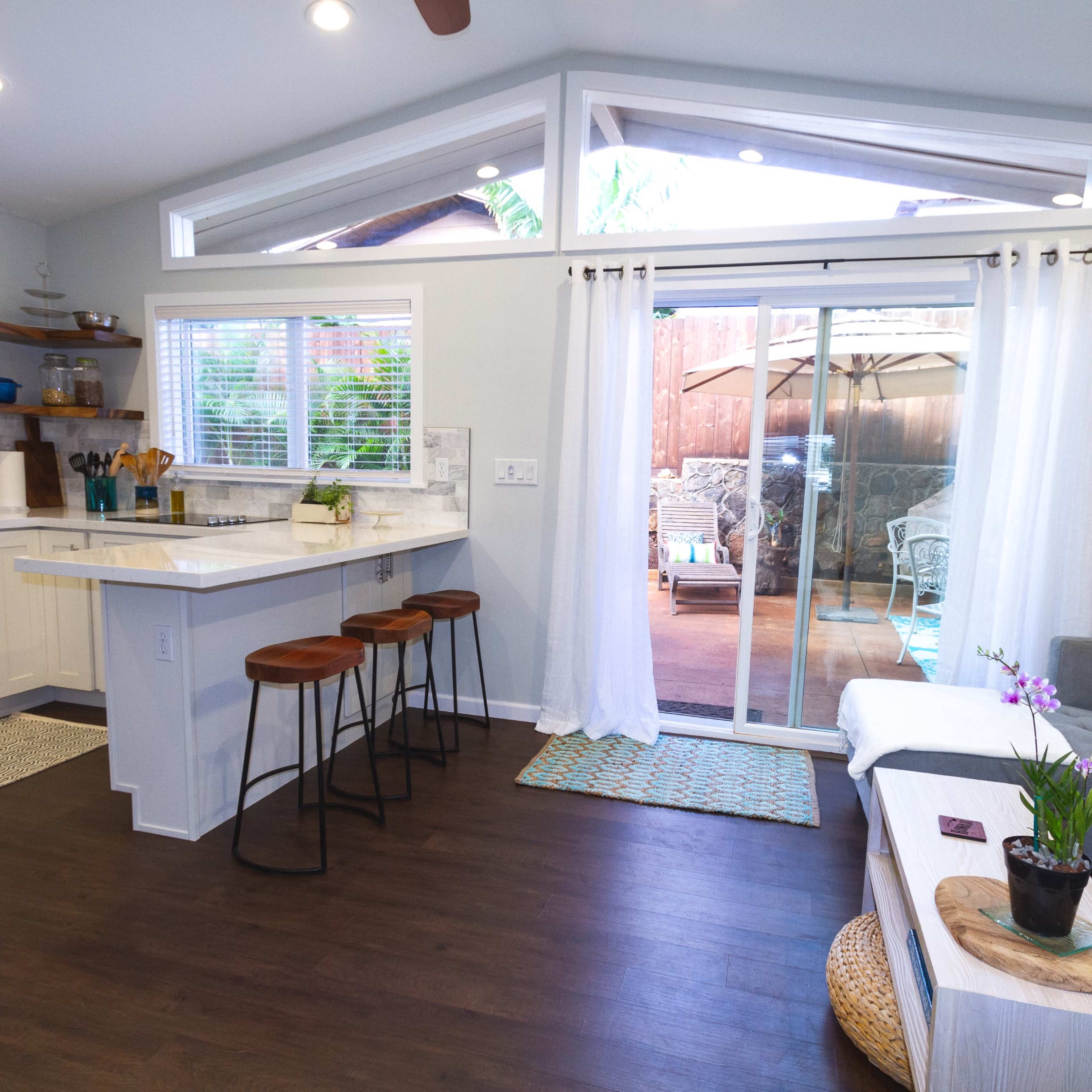A modern kitchen and living area with a bar space, sliding glass doors leading to an outdoor patio, and a small potted plant on a coffee table.