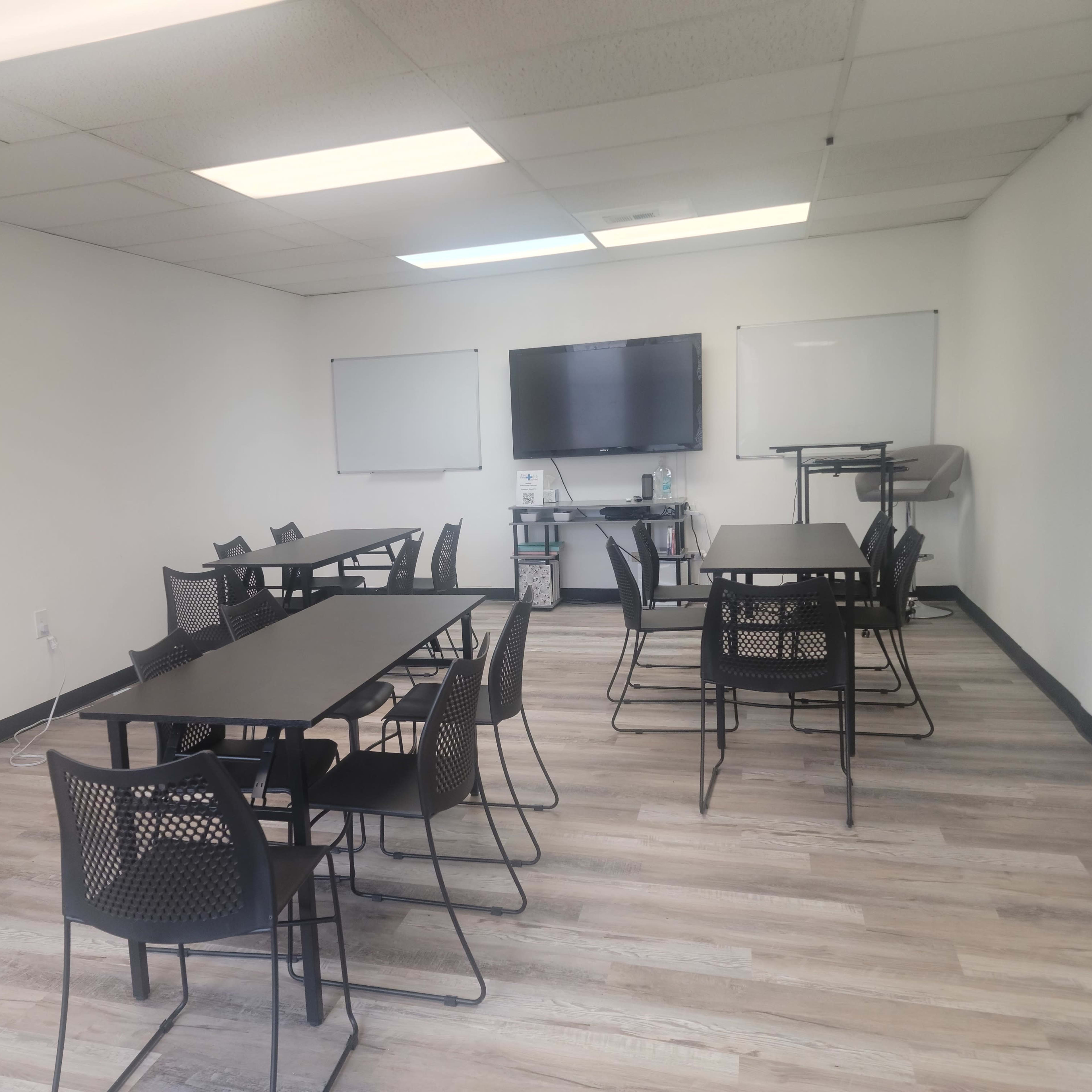 A light-filled meeting room features several tables and chairs arranged for group discussions.