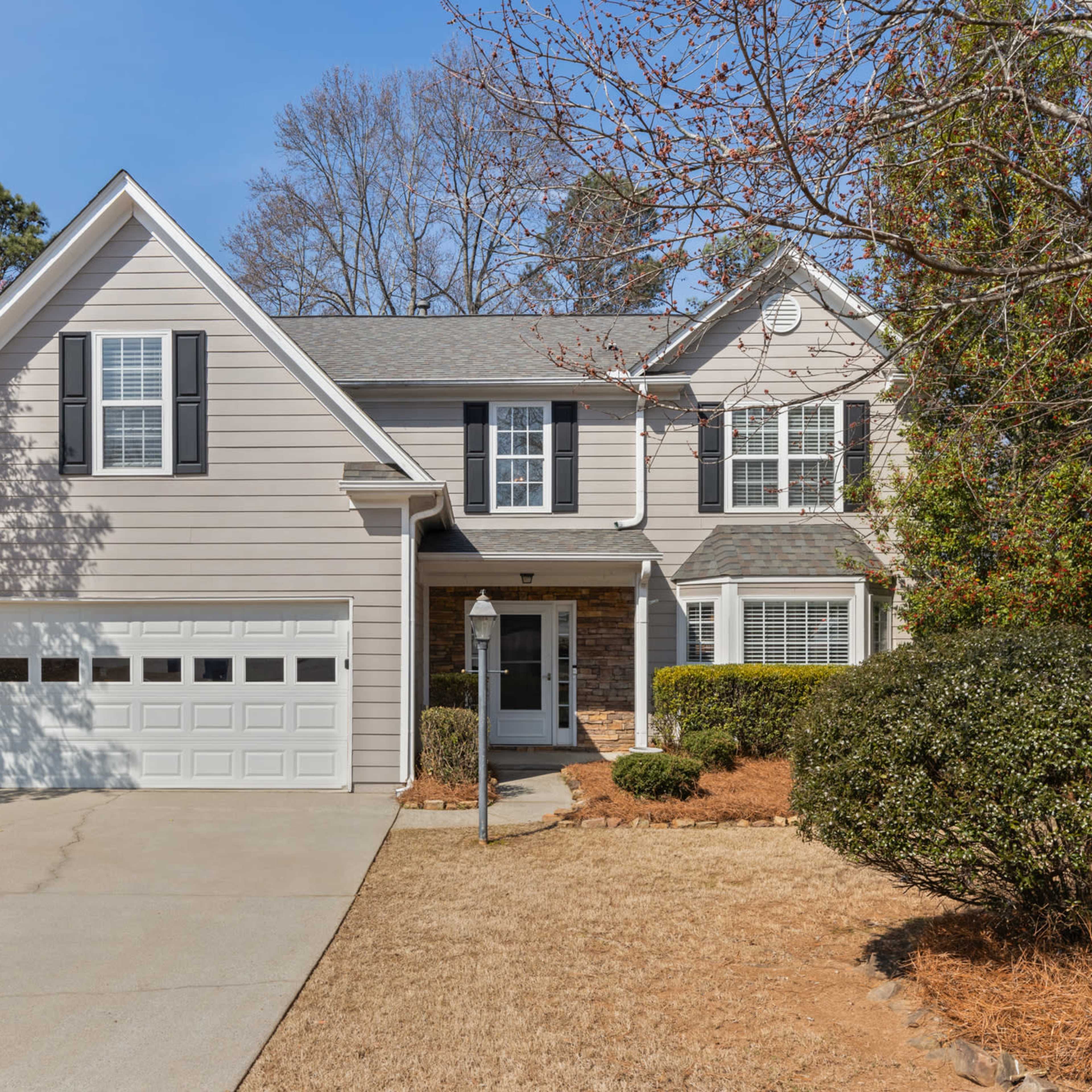 A two-story house with a light exterior, front porch, and attached garage is set in a landscaped yard.