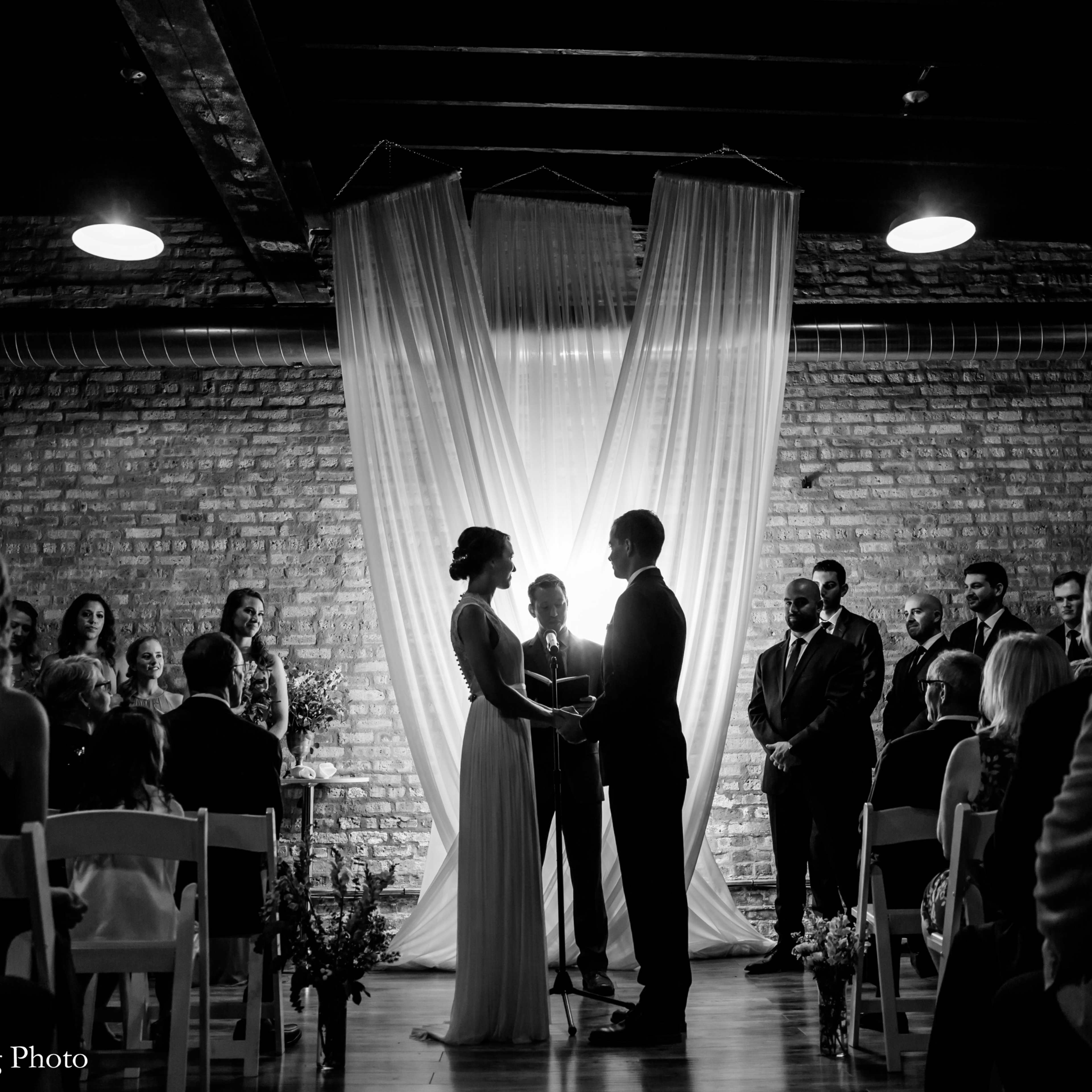A couple stands facing each other under flowing fabric drapes during their wedding ceremony, surrounded by seated guests.