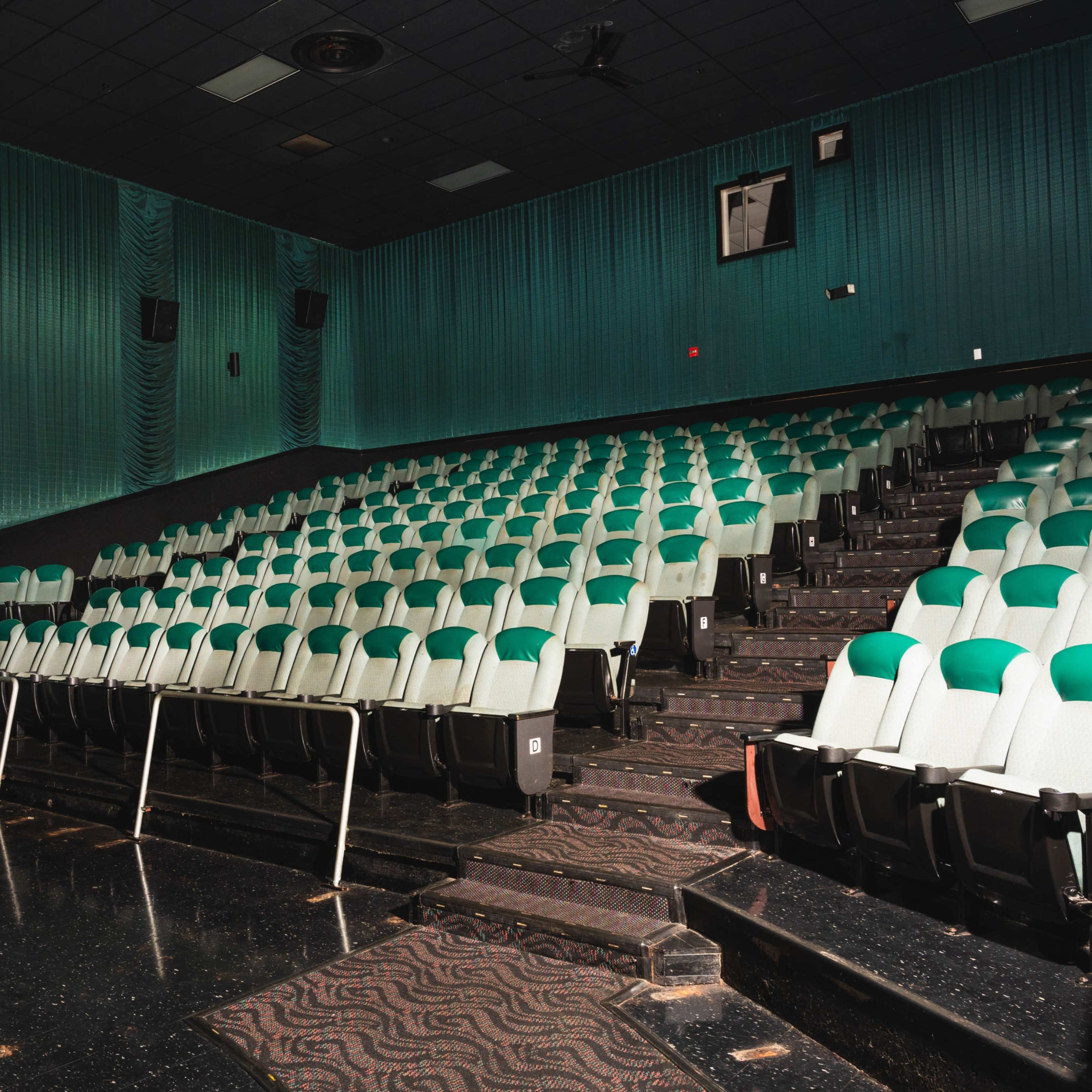 A movie theater with empty green and white seats arranged in rows on a dark carpeted floor.