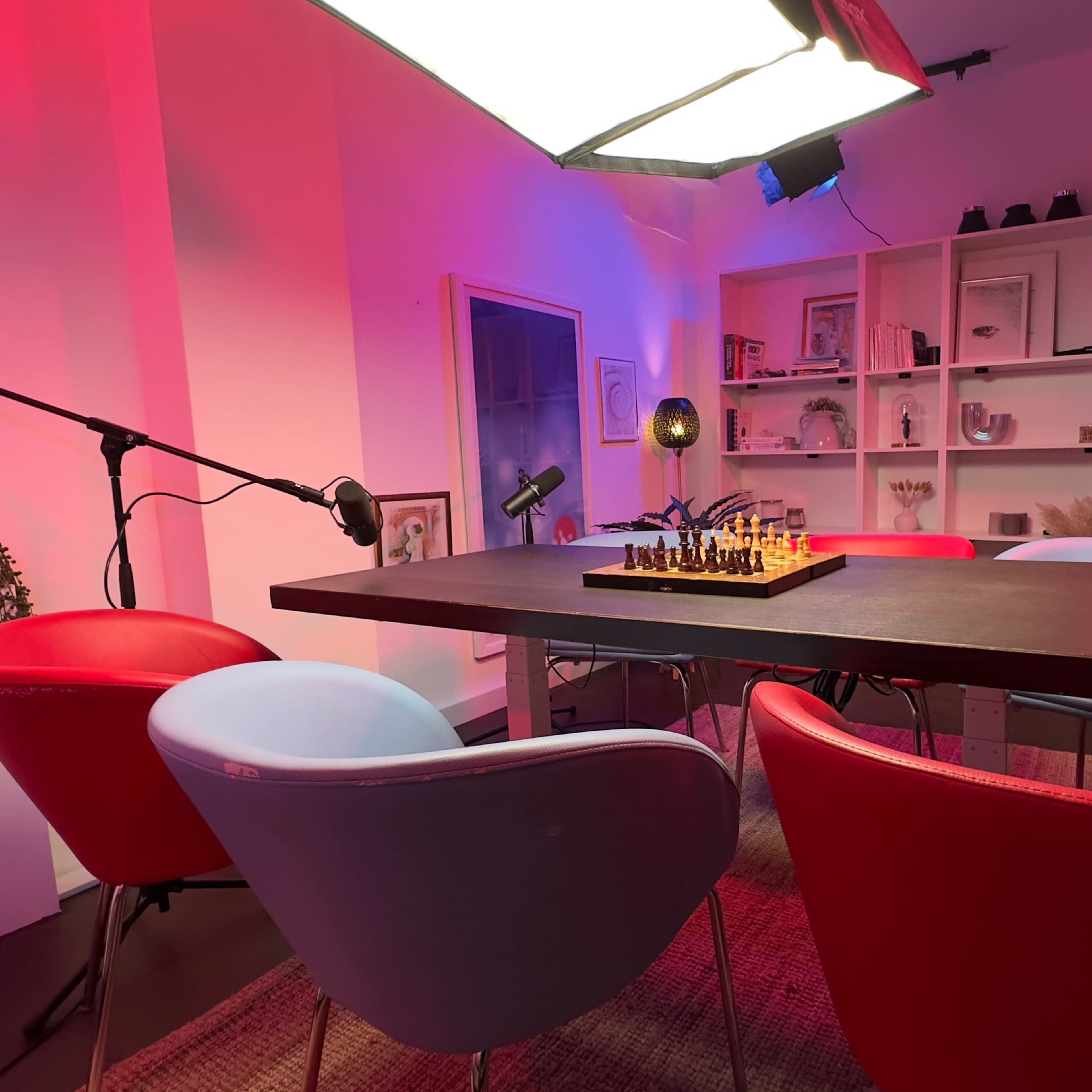 A table with a chessboard is set in a well-lit room featuring colorful chairs and a display shelf.