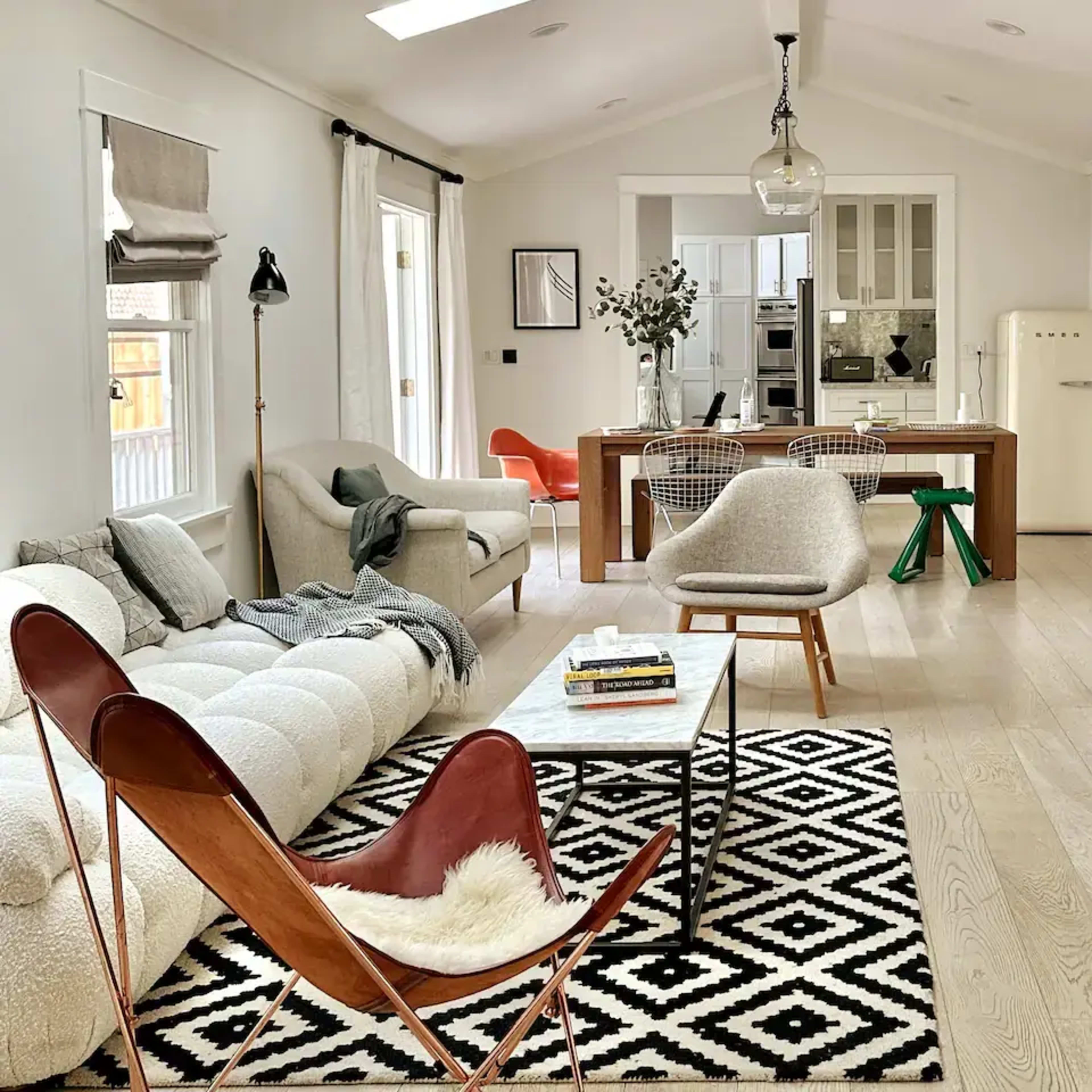 A modern living room with a white sofa, a black and white geometric rug, a wooden dining table, and various stylish furniture pieces.