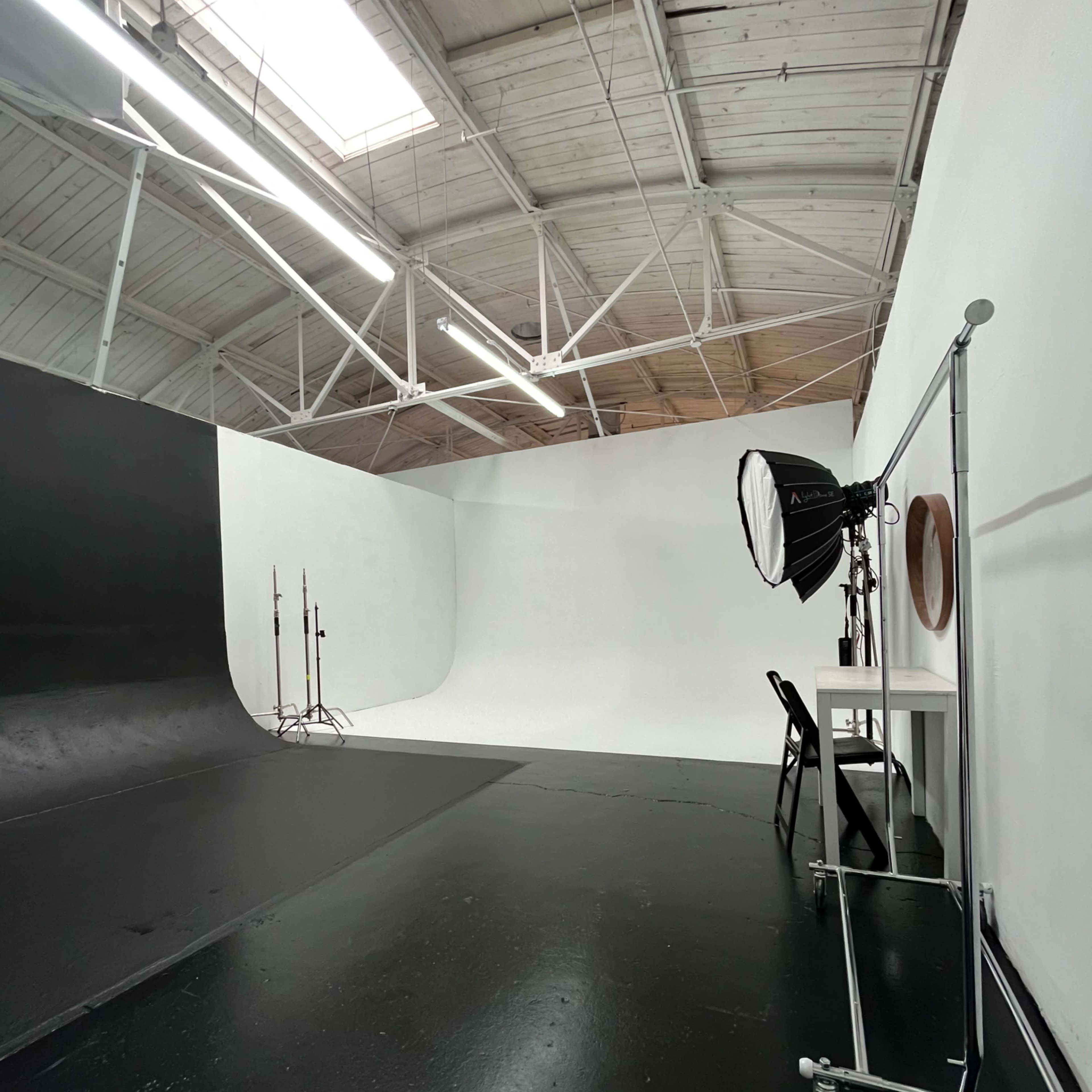 A photography studio featuring a black backdrop, a white curved backdrop, and a lighting setup.