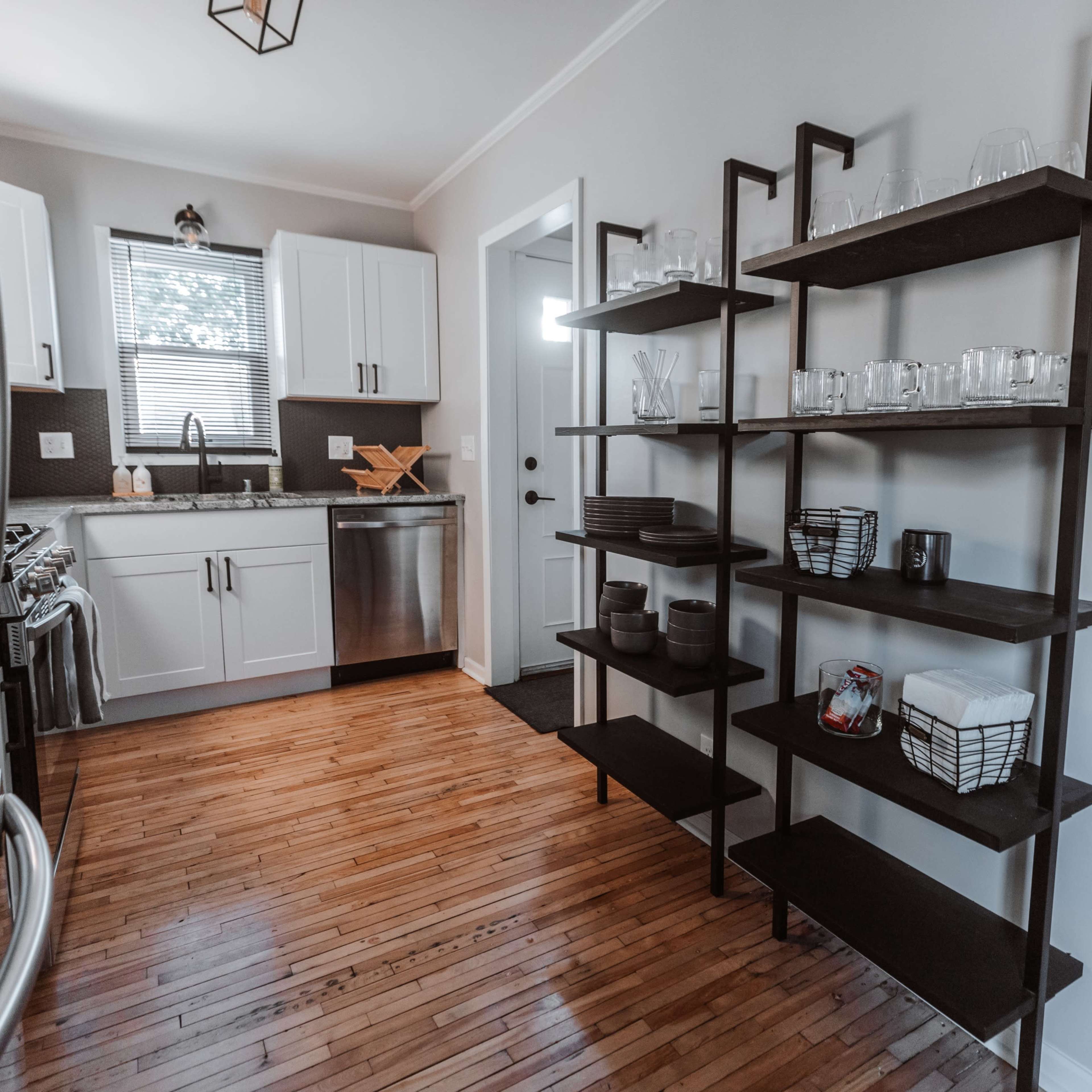 A modern kitchen with stainless steel appliances, a wooden floor, and open shelving displaying various glassware and kitchen items.
