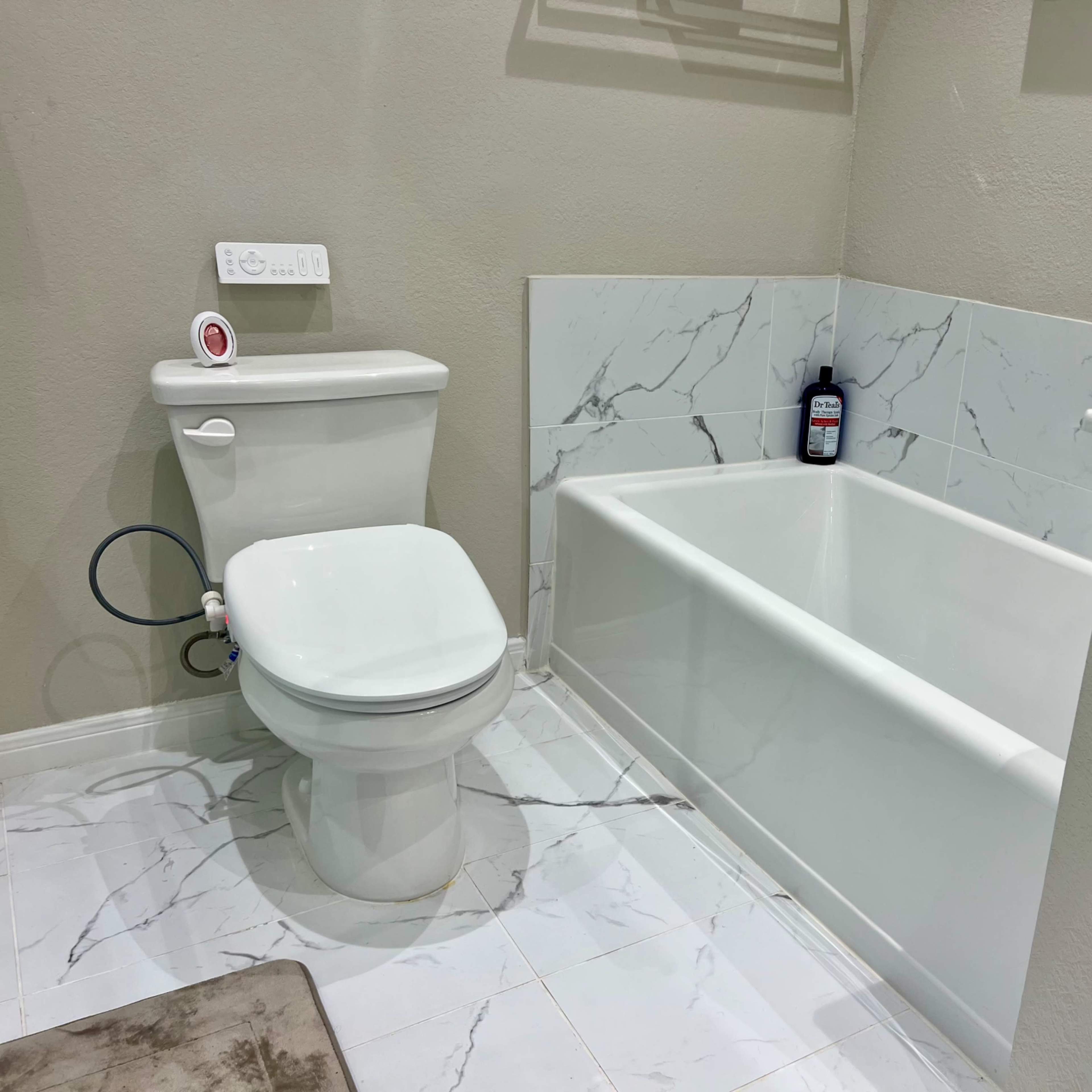 A bathroom featuring a white toilet, a bathtub, and marble-patterned walls.